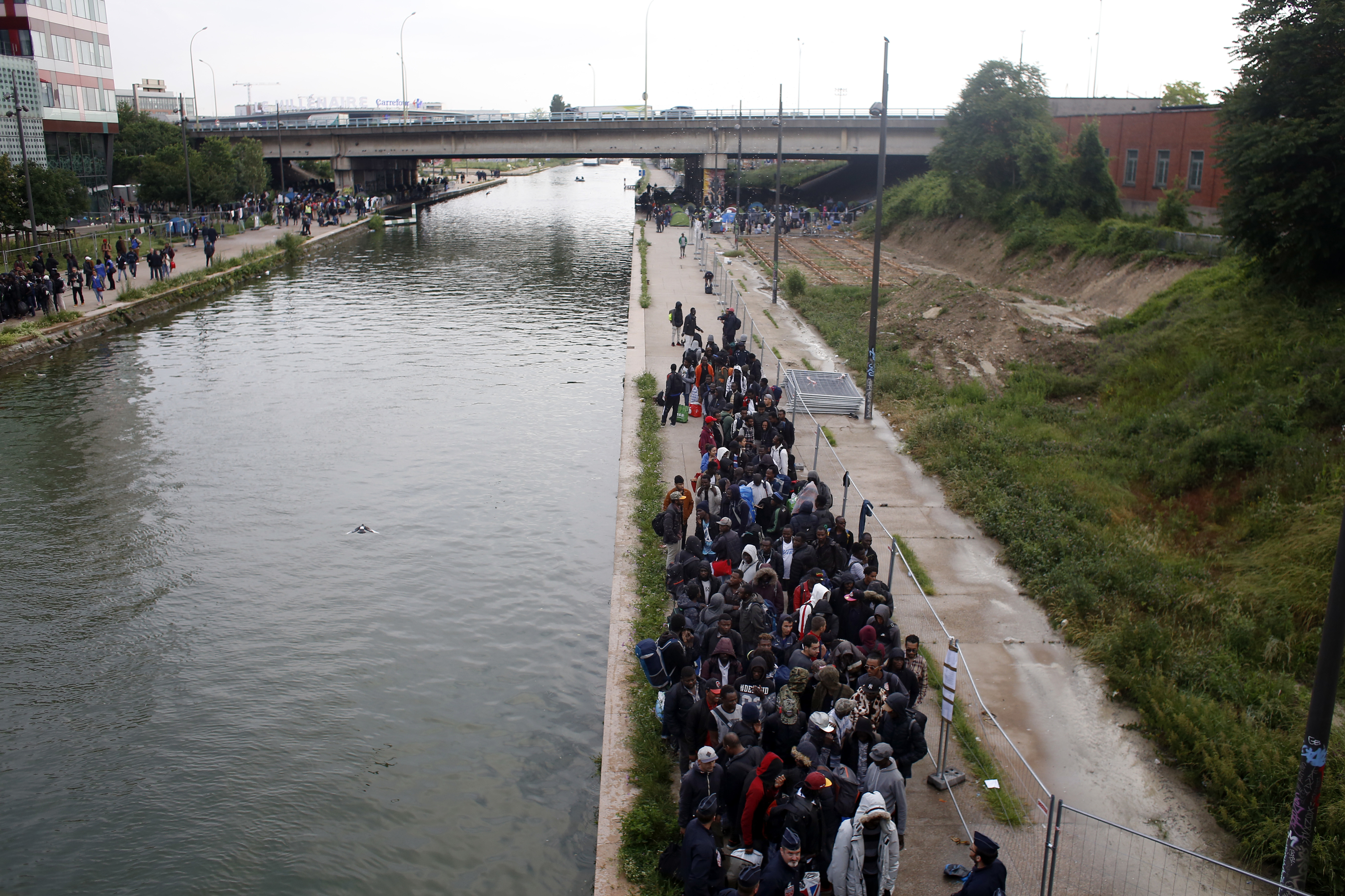 Migrants line up in a makeshift camp during its evacuation in Paris