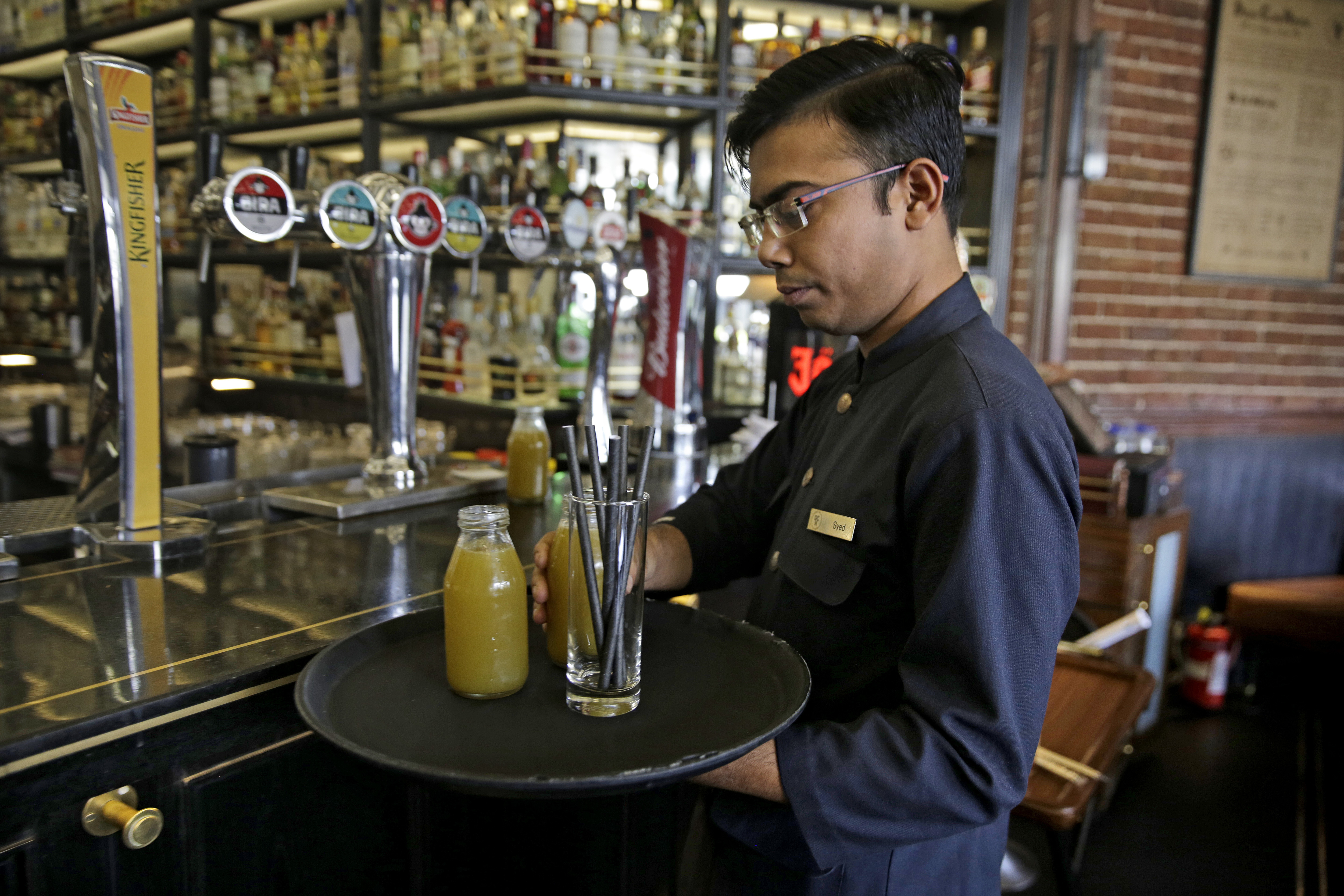 A waiter prepares to serve a drink with paper straws and drinks on his plate at Delhi Club House restaurant