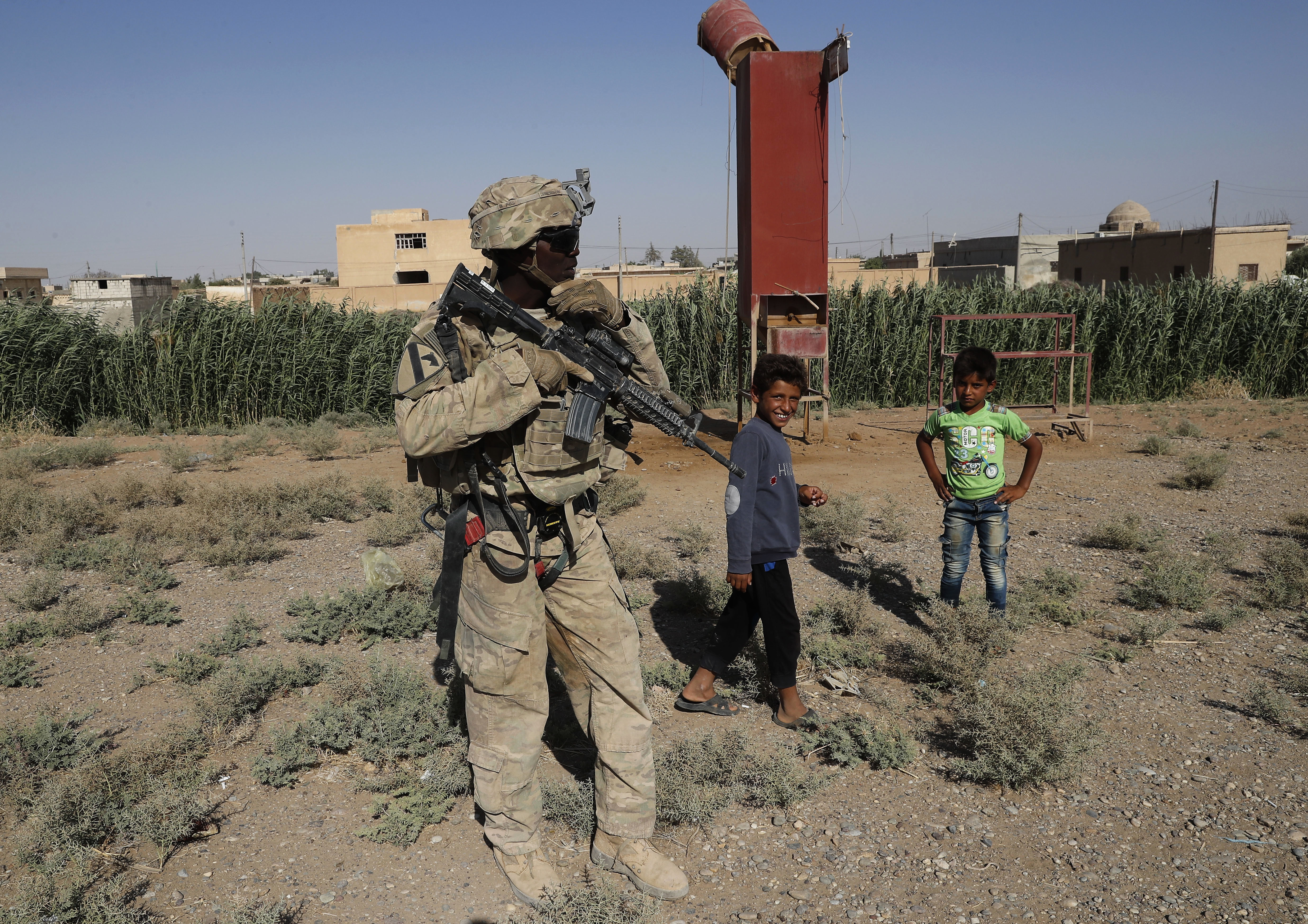 A US soldier stands near Syrian children on a road that leads to Raqqa 