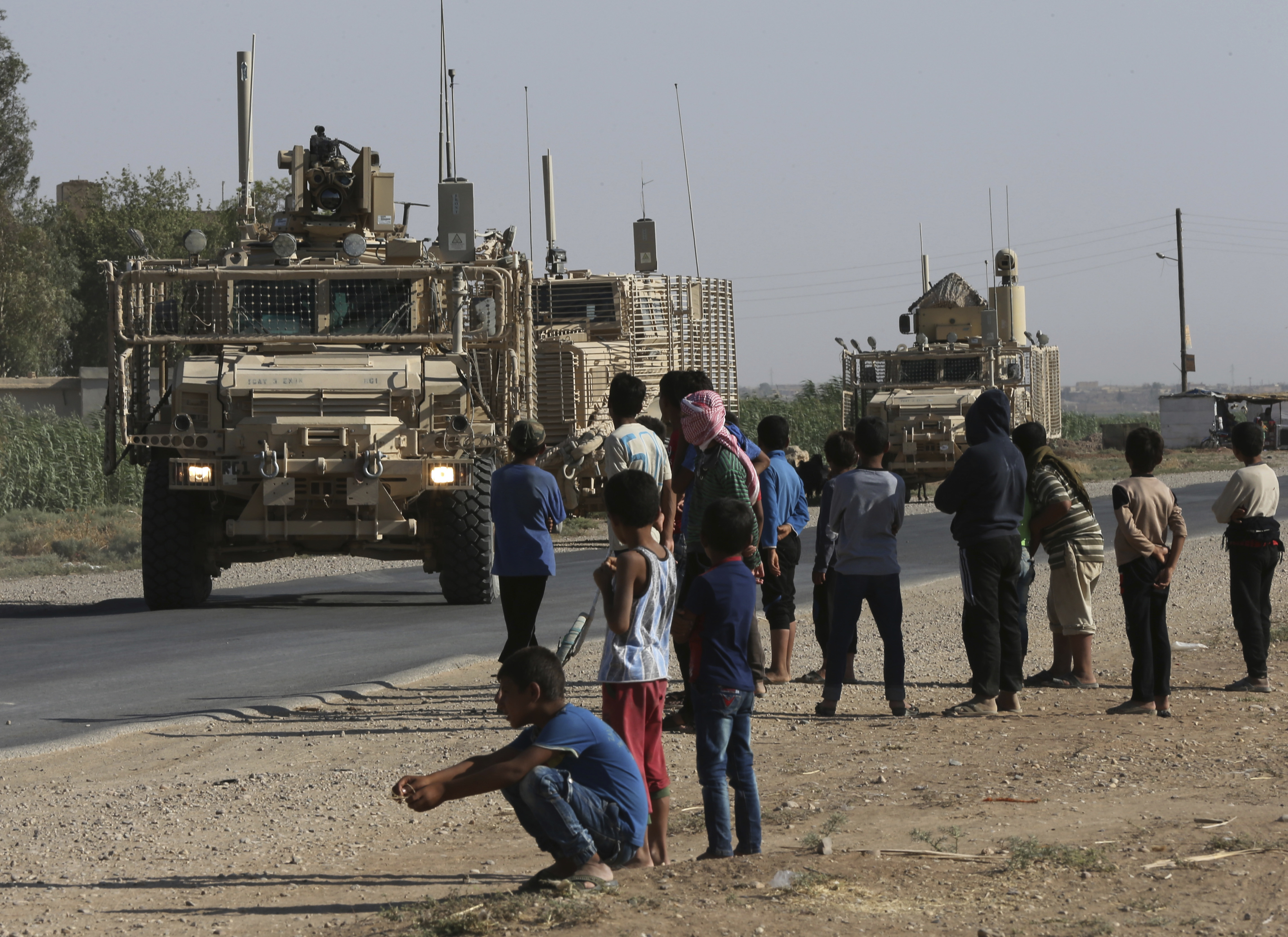 Syrians look at a US armoured vehicle convoy on a road that leads to Raqqa