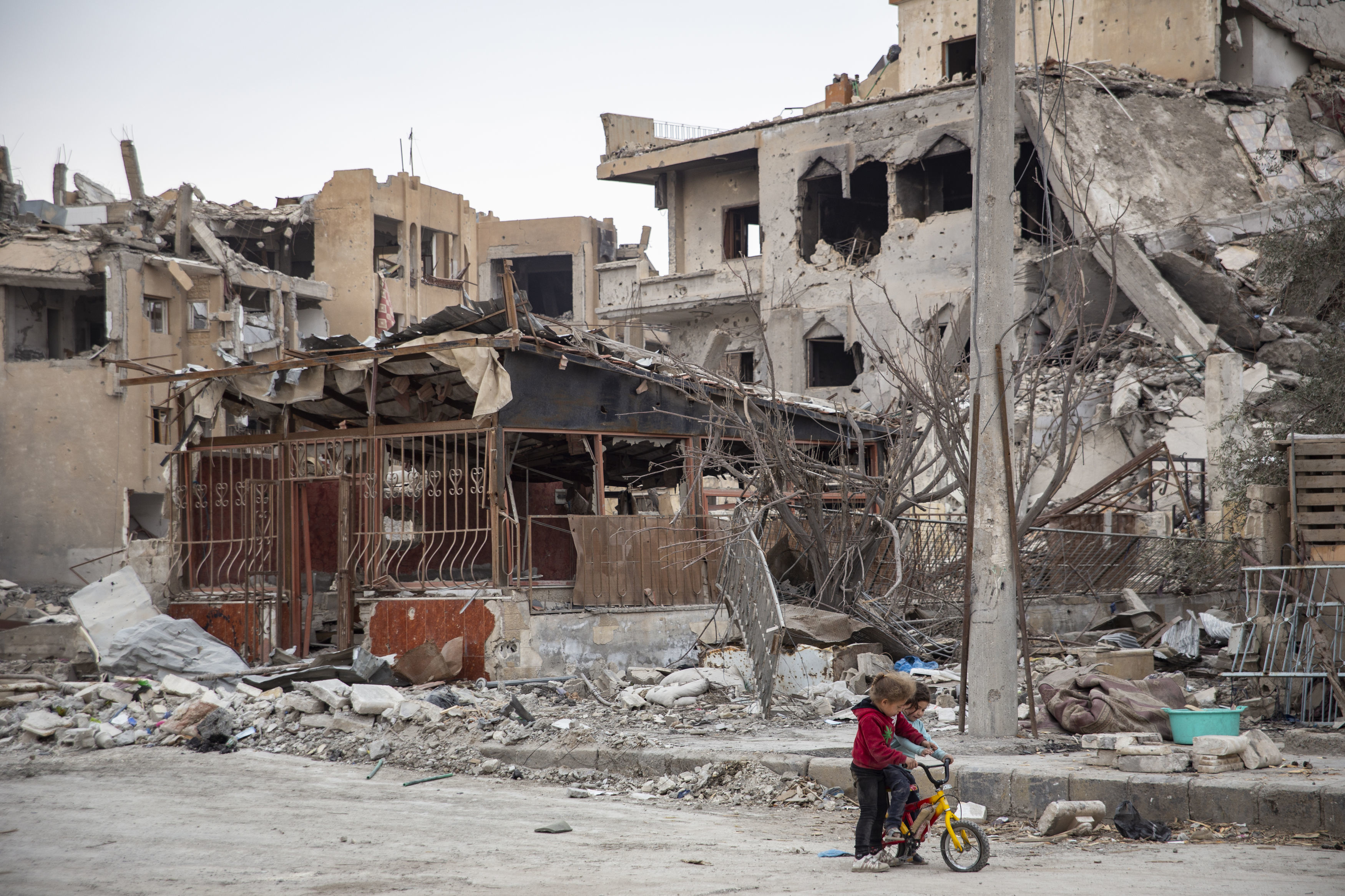 Children riding a bicycle next to destroyed buildings in Raqqa 