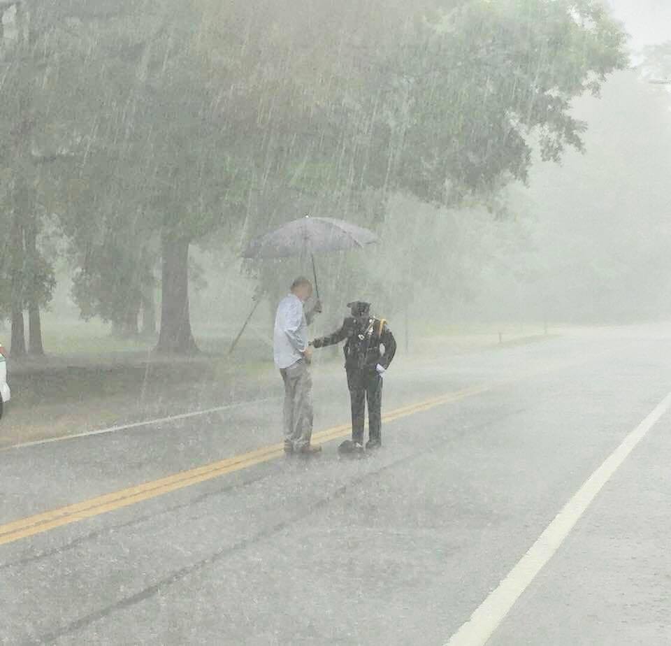 Mr Hammett holding an umbrella over an officer assisting a snapping turtle in heavy rain 