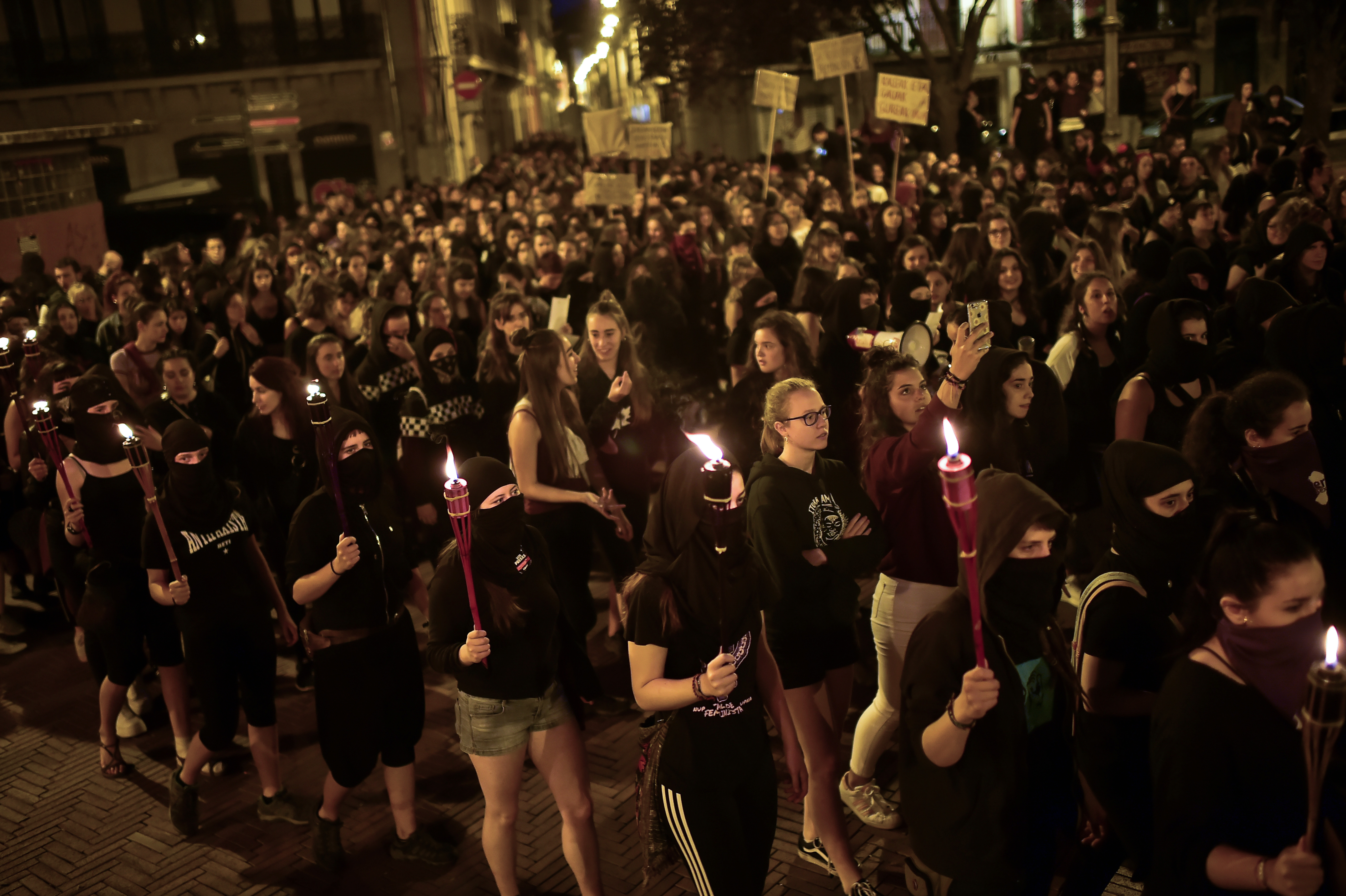 Women activists hold candles with their faces covered while taking part in a protest against male violence before the famous San Fermin festival in Pamplona