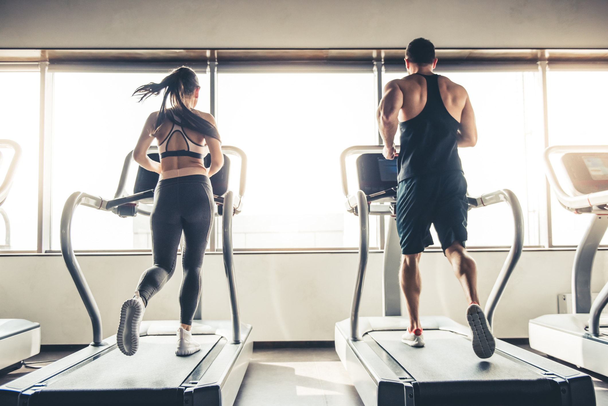 Back view of beautiful sports people running on a treadmill in gym