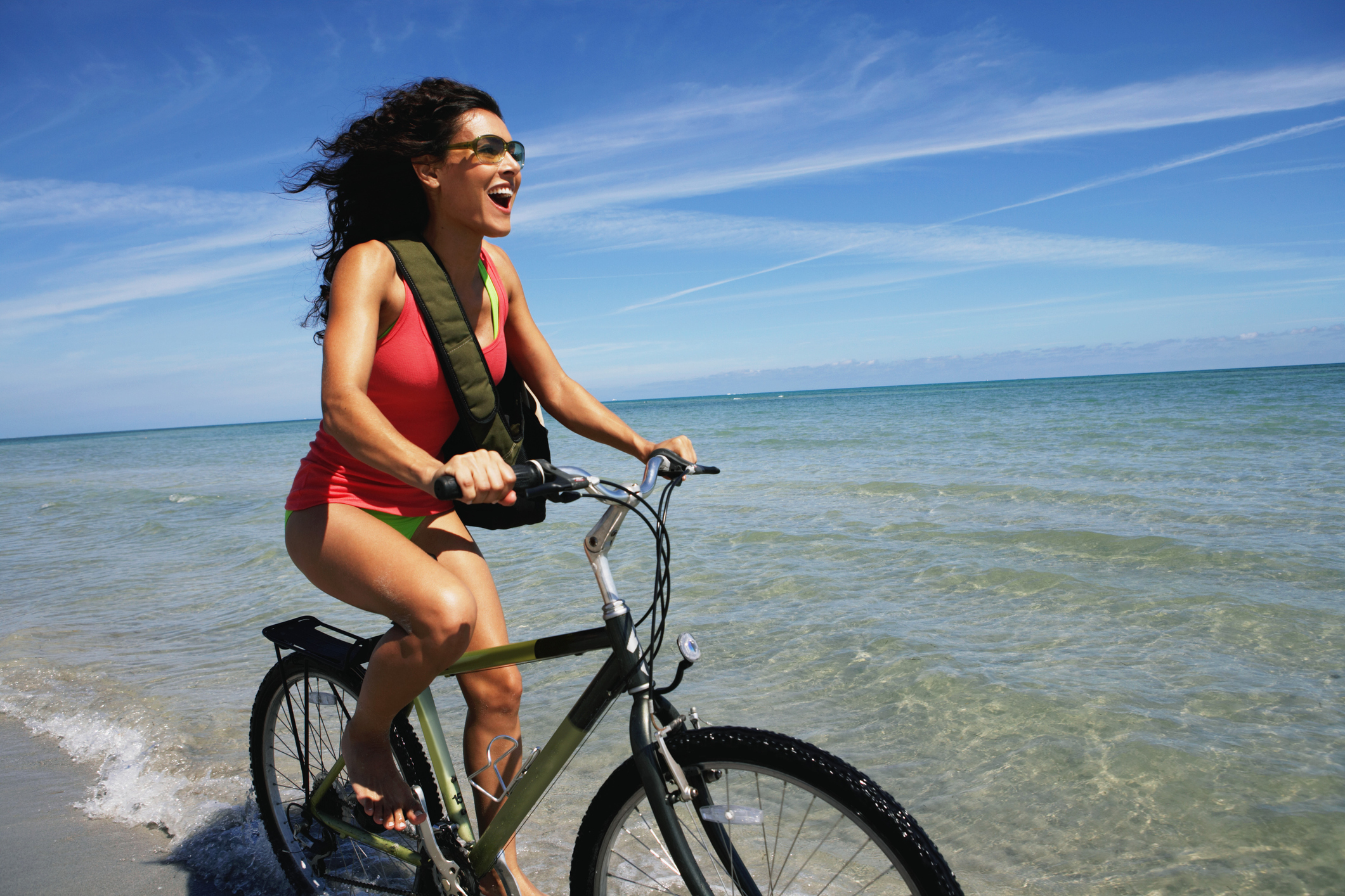 Young woman riding bicycle on beach, smiling, side view