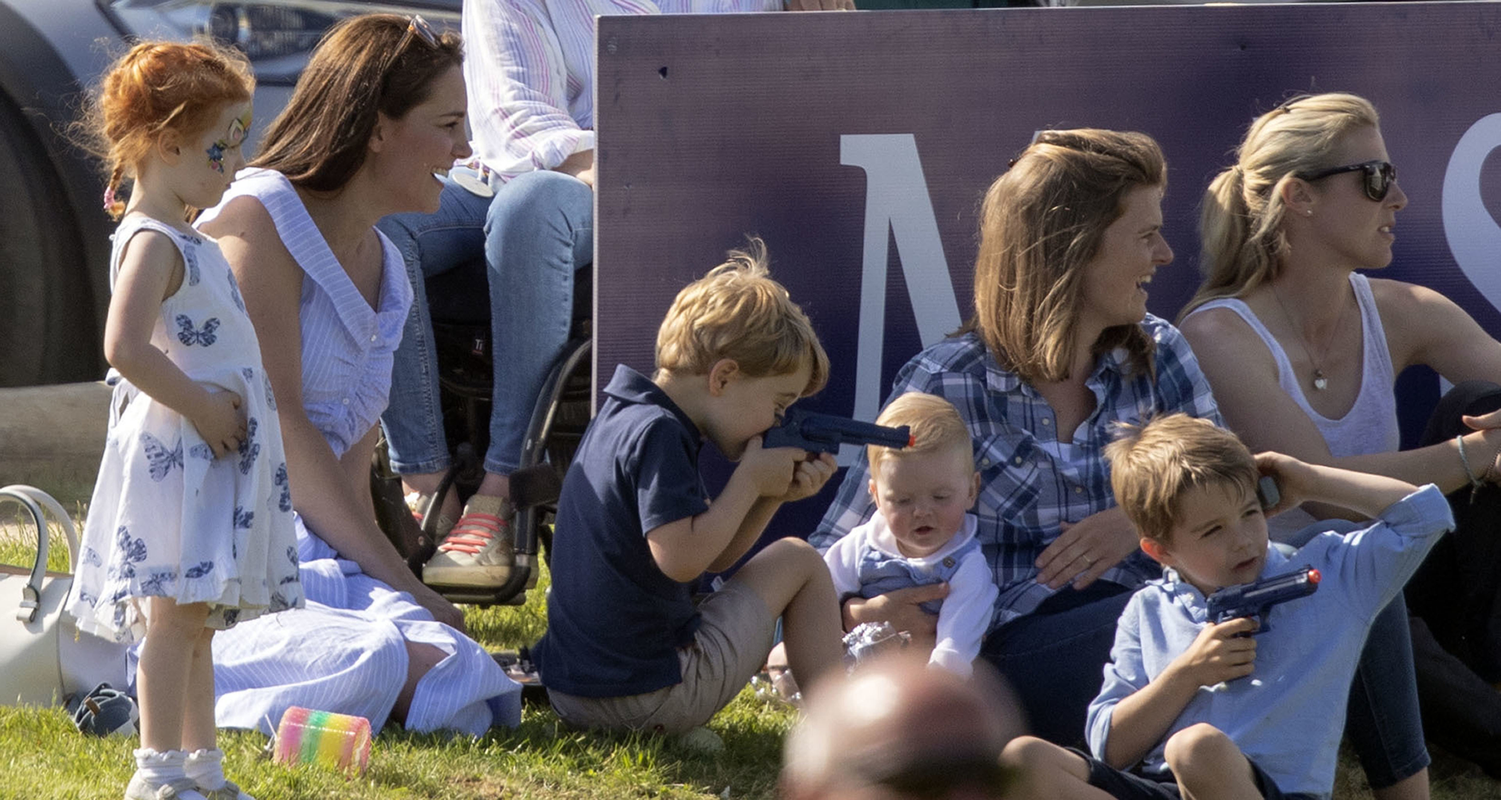 Prince George plays with a toy gun as he sits with his mother the Duchess of Cambridge (left), whilst his father the Duke of Cambridge takes part in the Maserati Royal Charity Polo Trophy at the Beaufort Polo Club, Downfarm House, Westonbirt, Tetbury