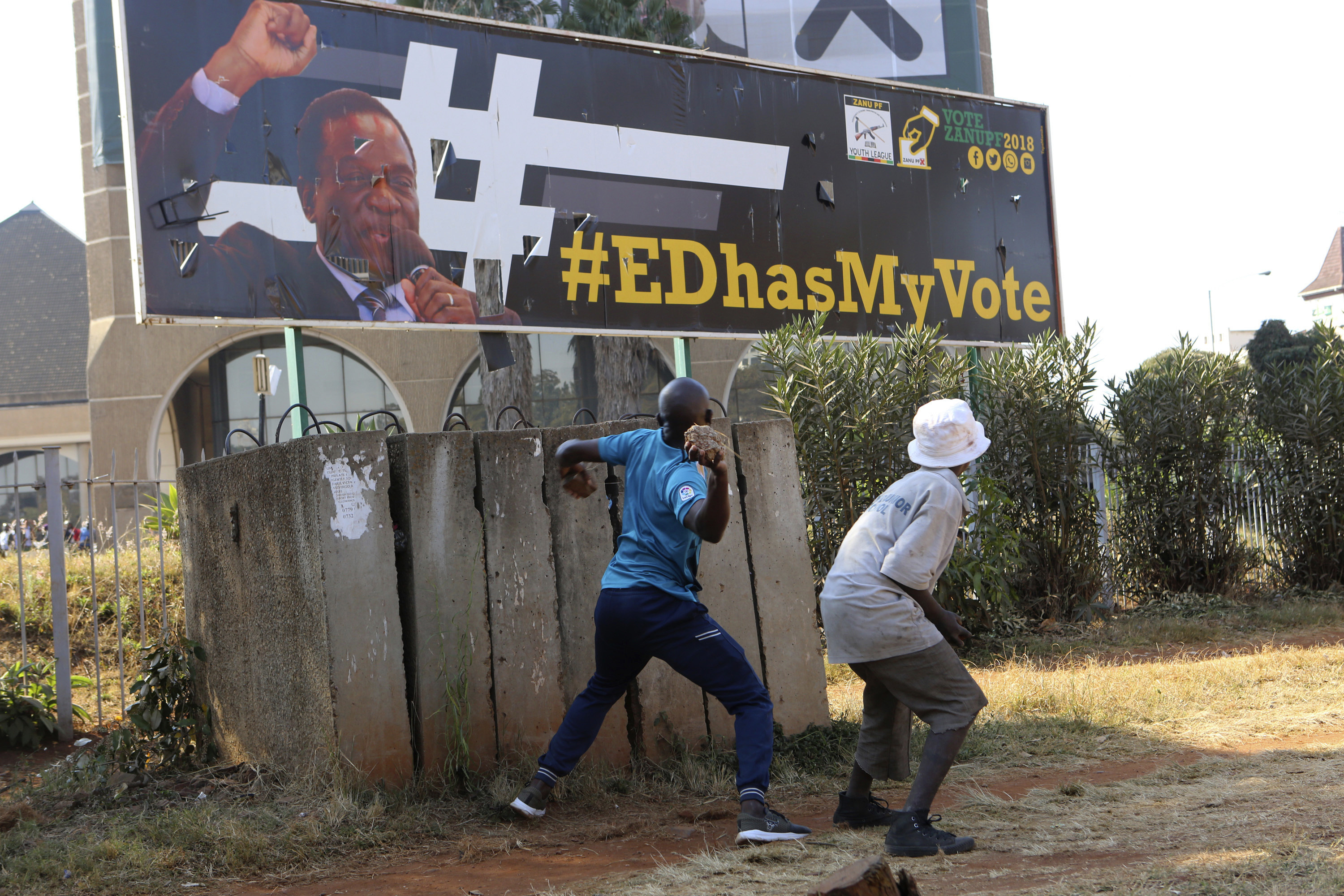 An opposition party supporter throws a rock aimed at Zimbabwean President Emmerson Mnangagwa's election campaign poster in Harare