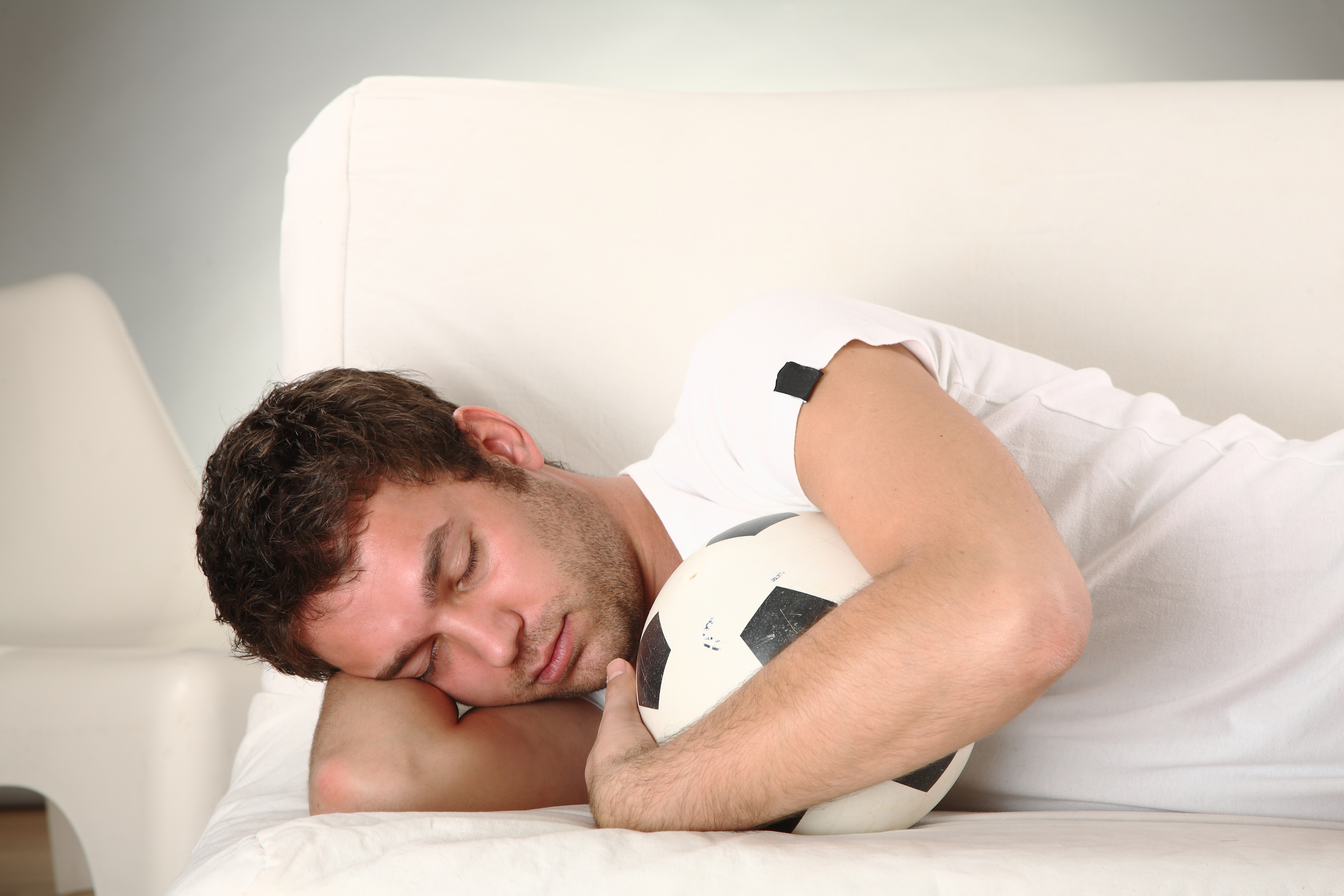 A man sleeps on a sofa with a football