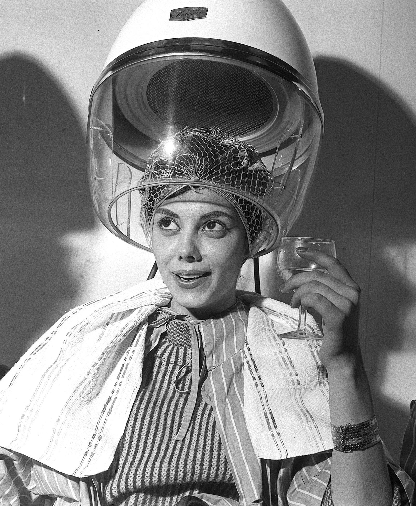 a woman under a hood hair dryer in the 1960's