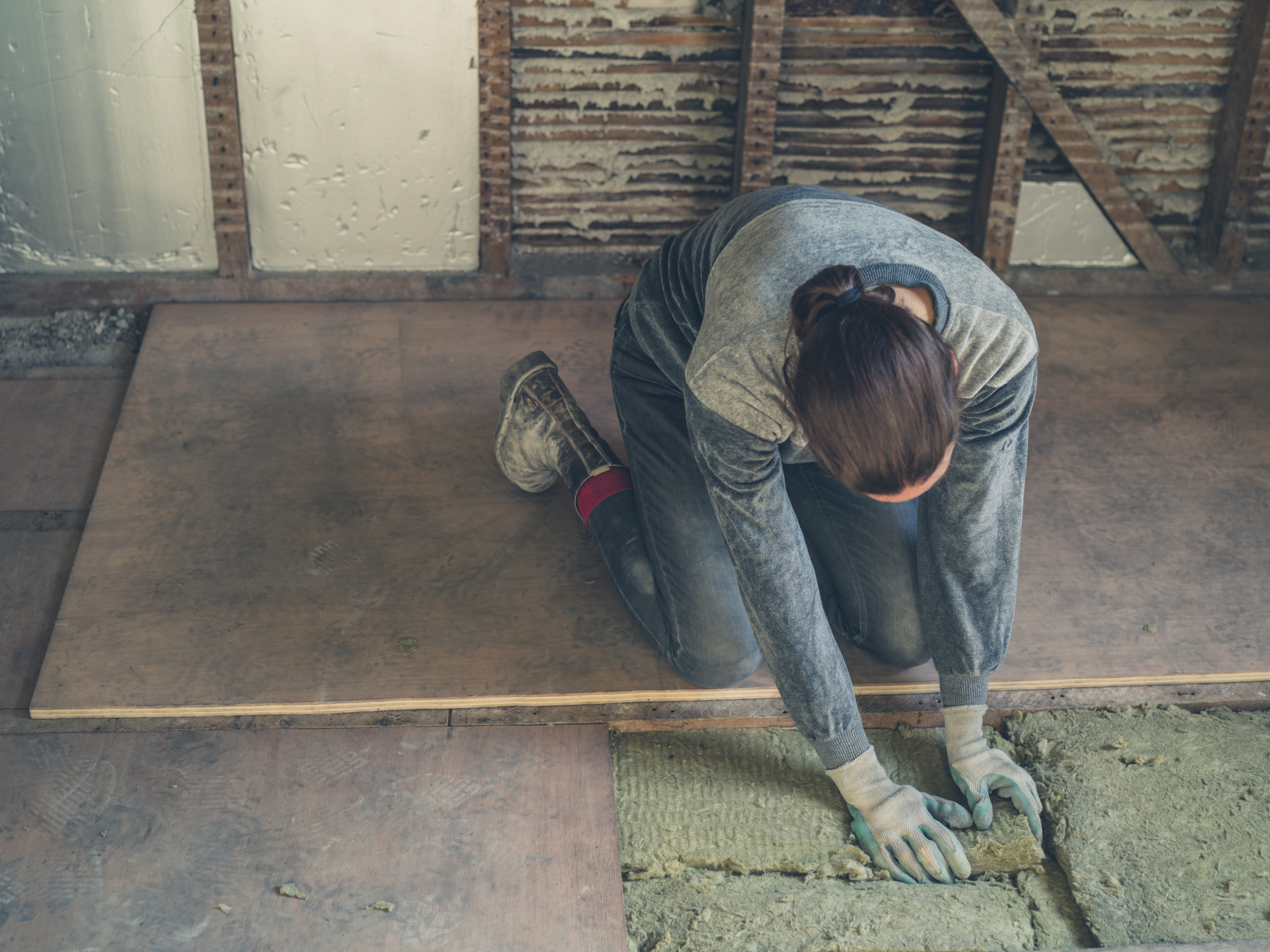 A young woman is laying down insulation in a loft