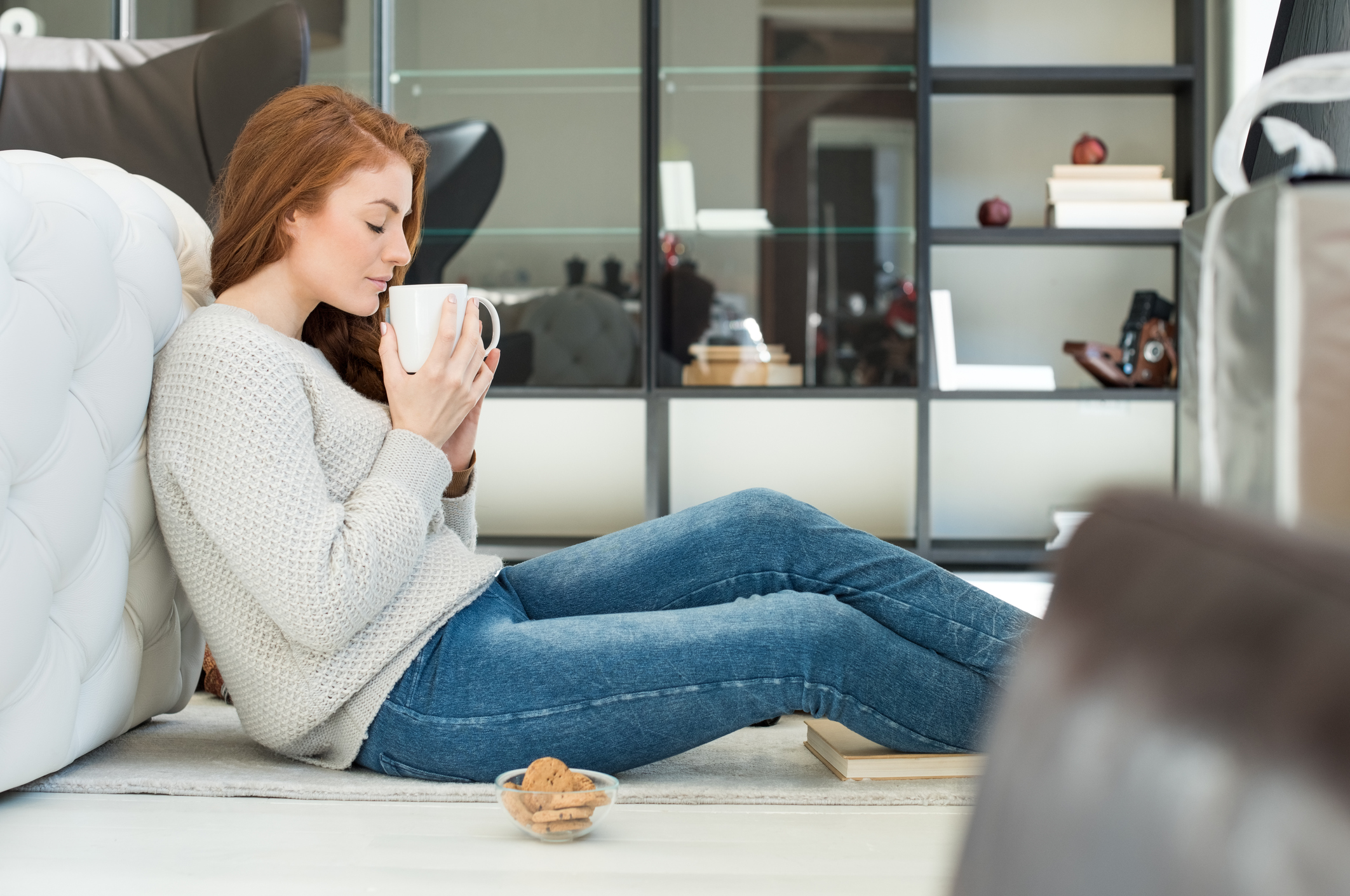 Side view of a young beautiful woman dirking hot tea with cookies. Beautiful woman relaxing while drinking tea in the afternoon. Serene young woman sitting on floor and smeeling a cup of tea.