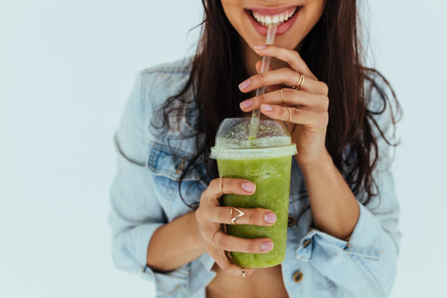 Close up of smiling woman drinking fresh juice with straw on white background. Female having a glass of fruit juice and smiling.