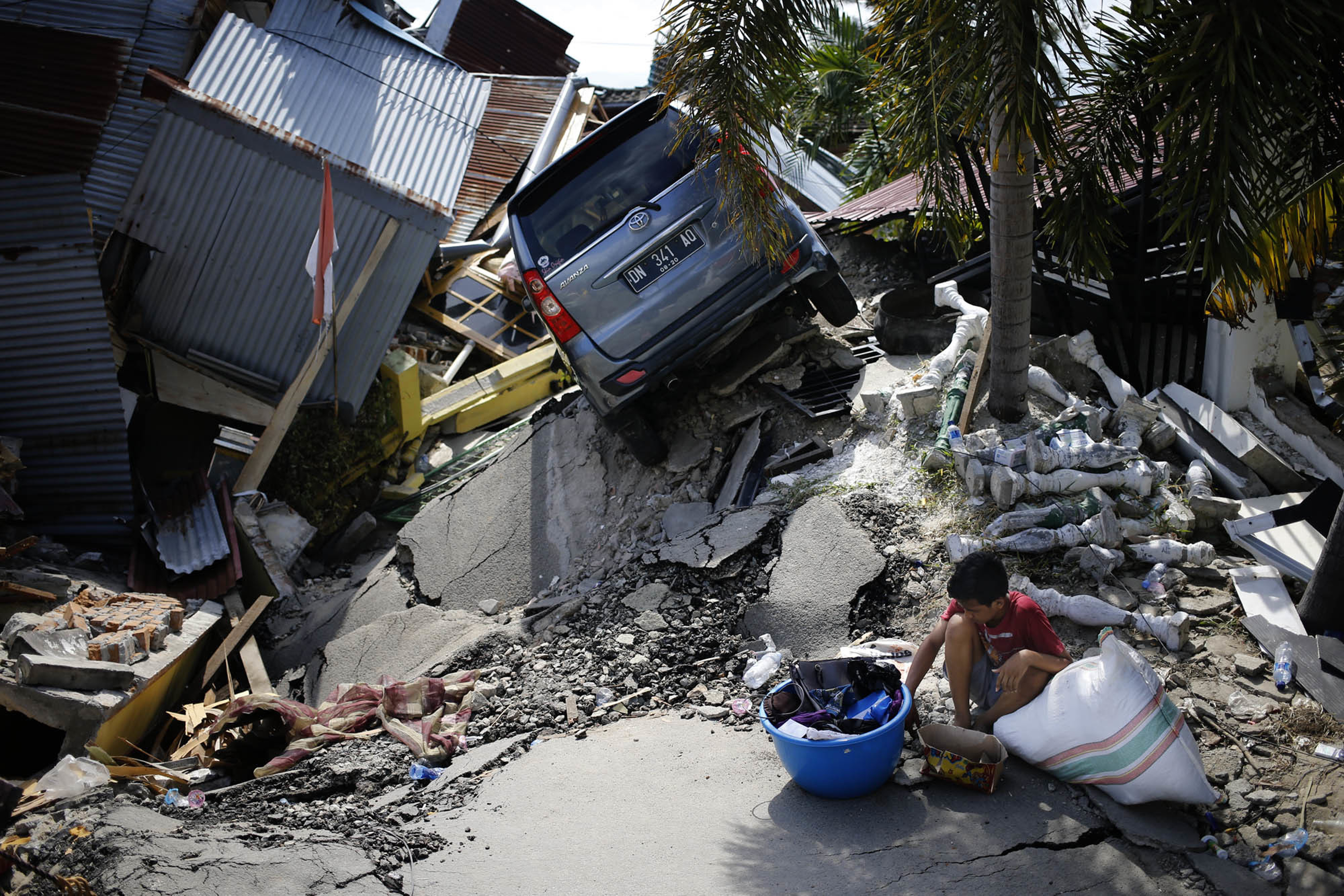 A boy sits with items salvaged from the ruins of a family member's house in the Balaroa neighbourhood in Palu