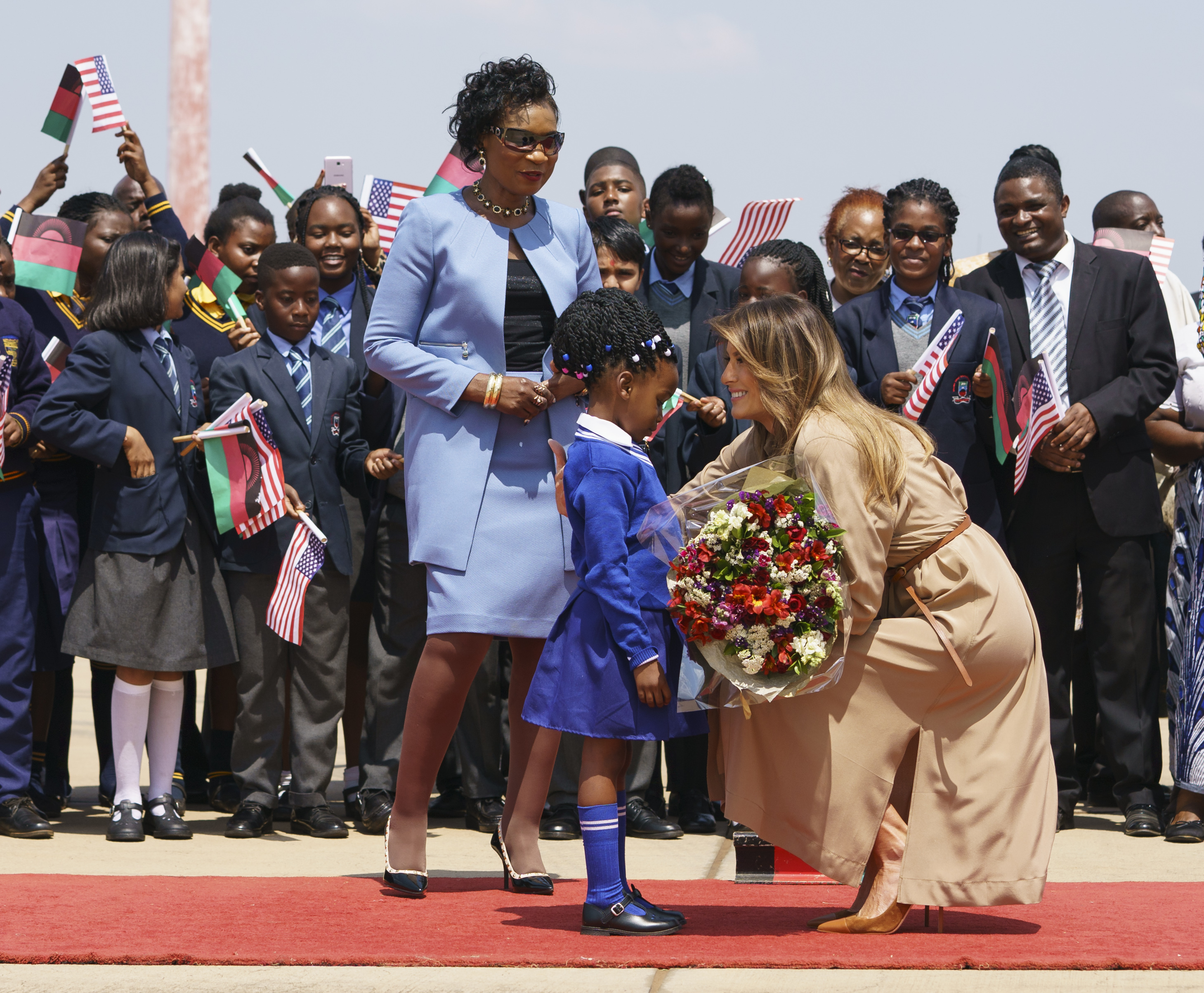 Melania Trump is greeted by Malawi first lady Gertrude Maseko and a flower girl as she arrives at Lilongwe International Airport 