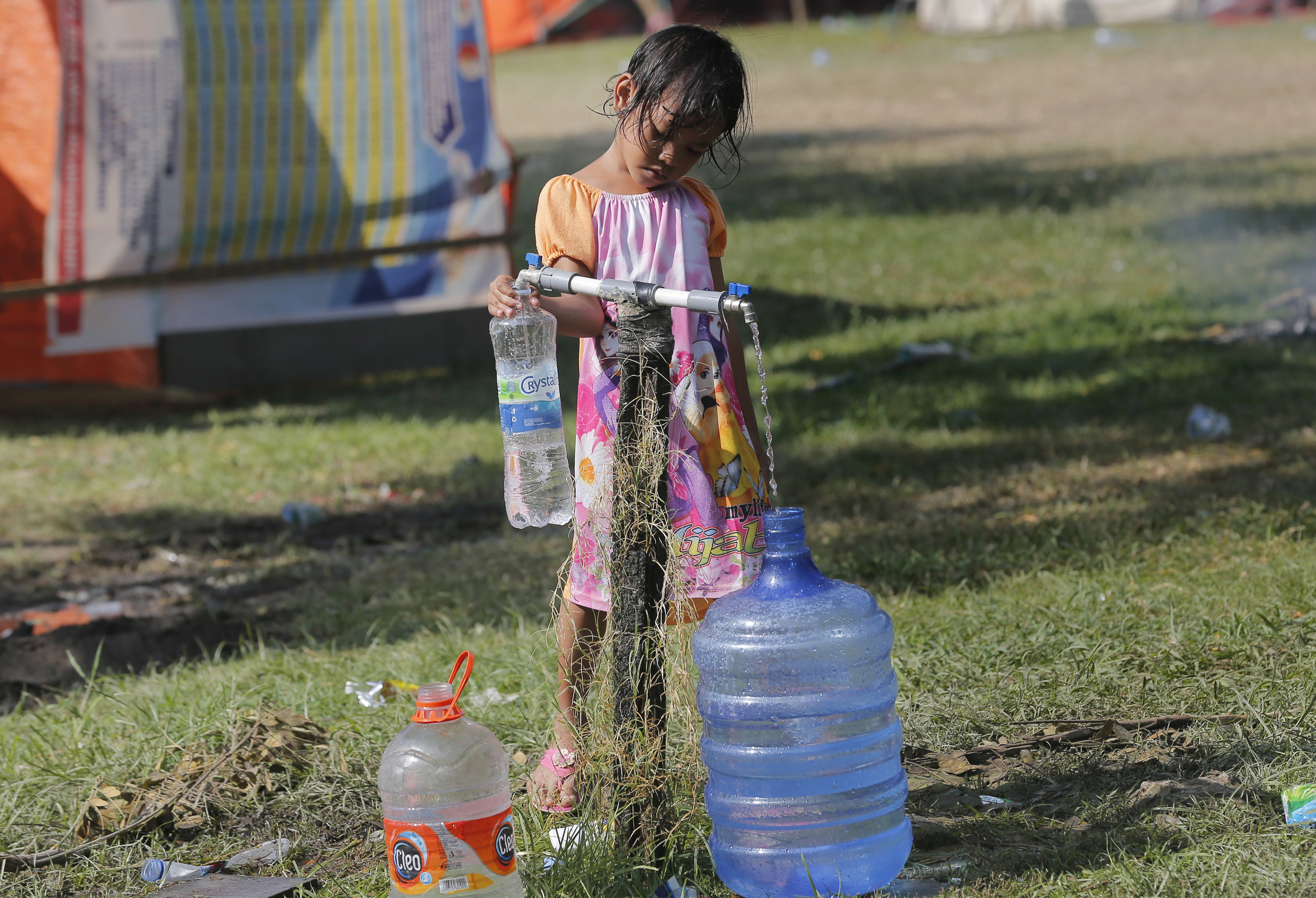A girl fills water jugs at a temporary shelter in Palu