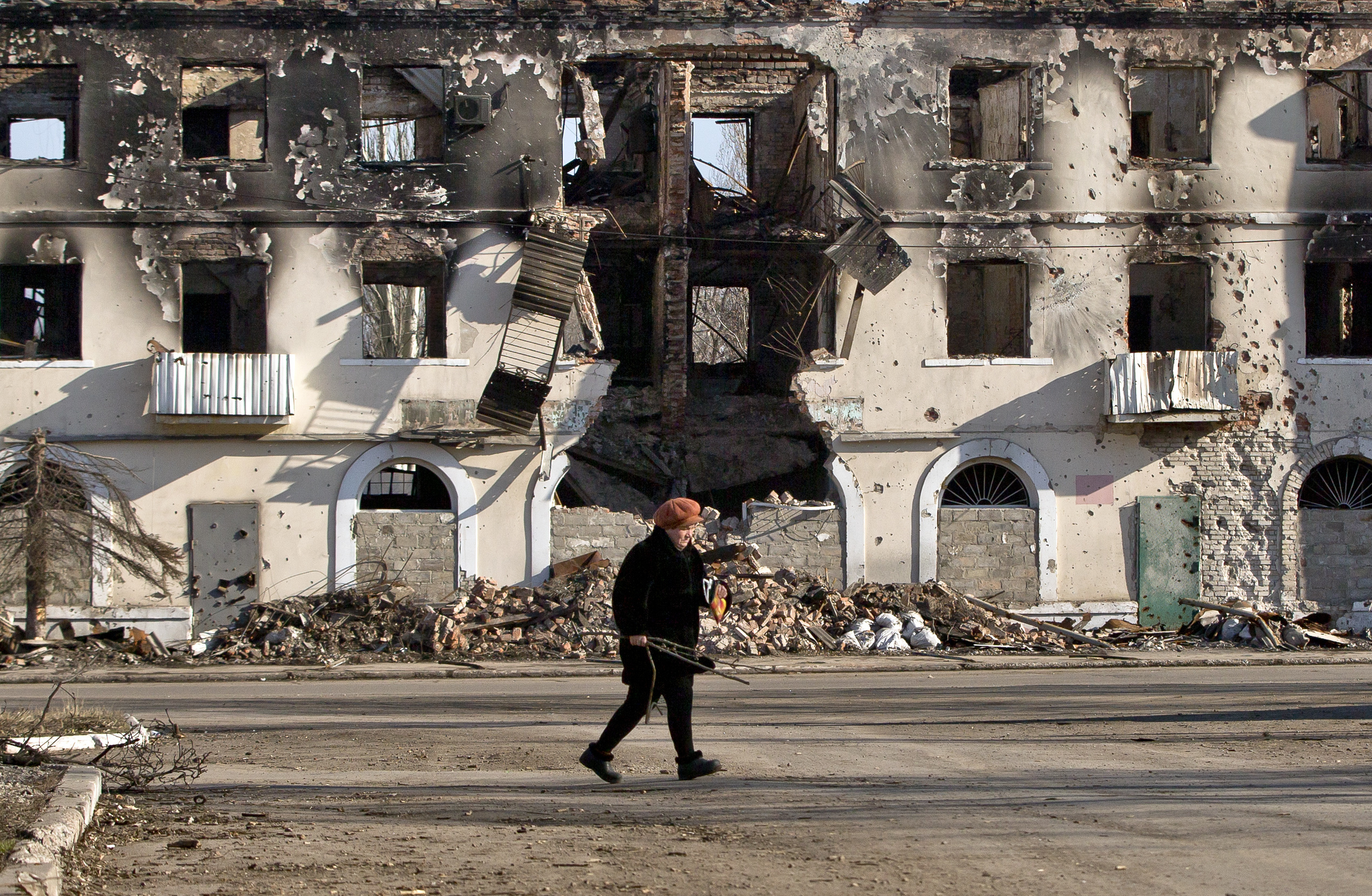 An elderly woman walks by a destroyed building in Vuhlehirsk, Ukraine, in 2015
