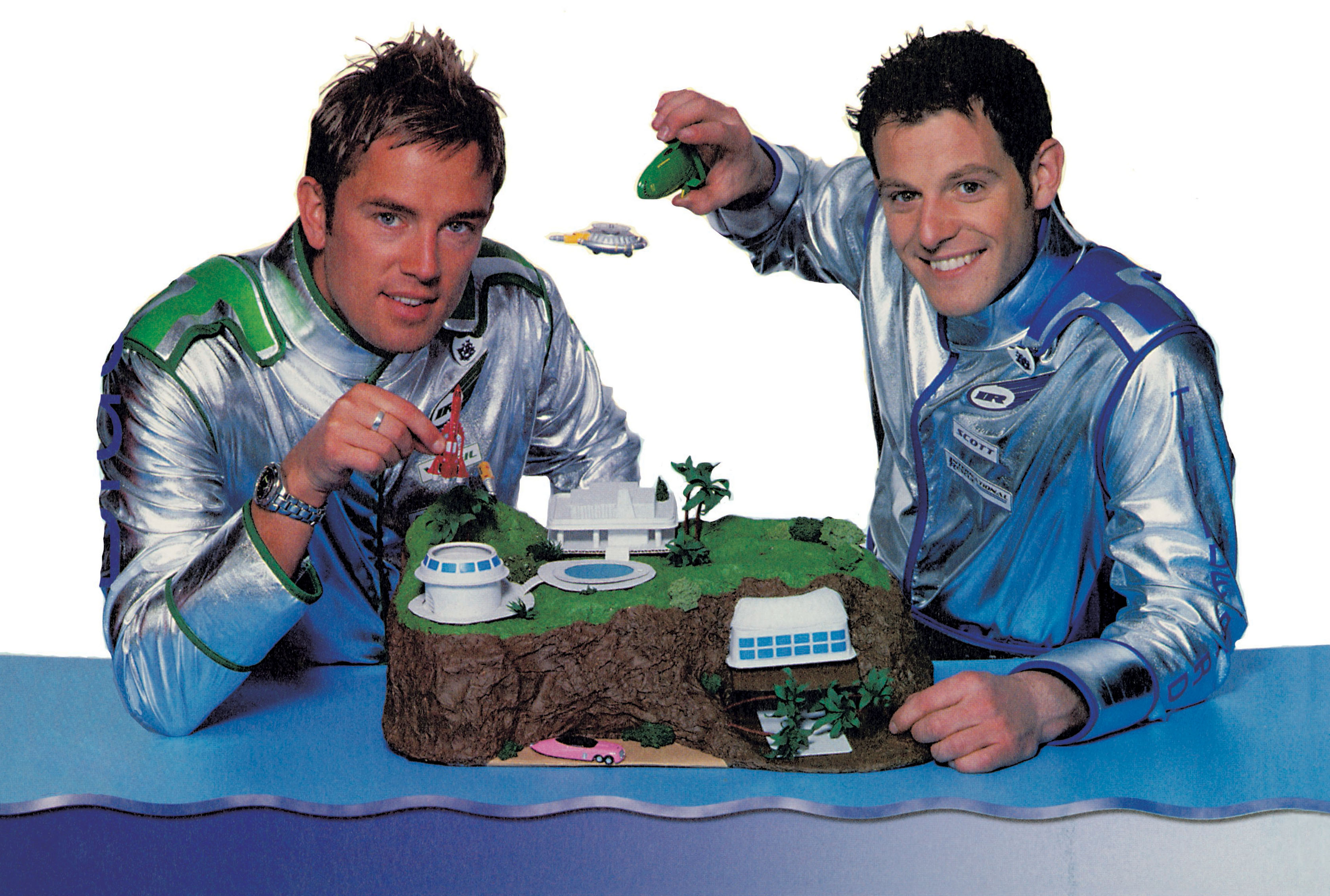 Two presenters play with a model of Tracy Island