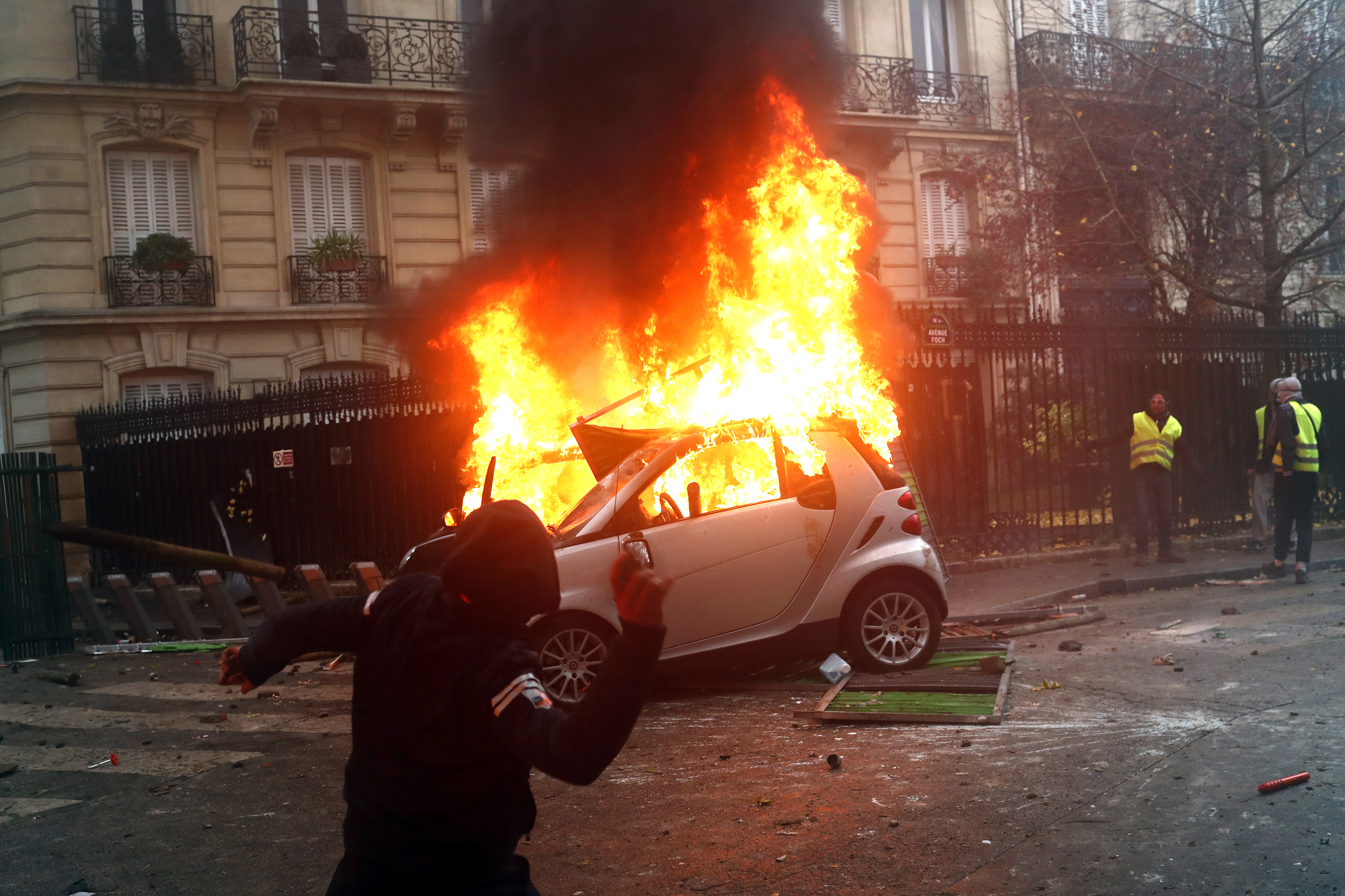 A hooded demonstrator throws an item as a car burns during a demonstration in Paris