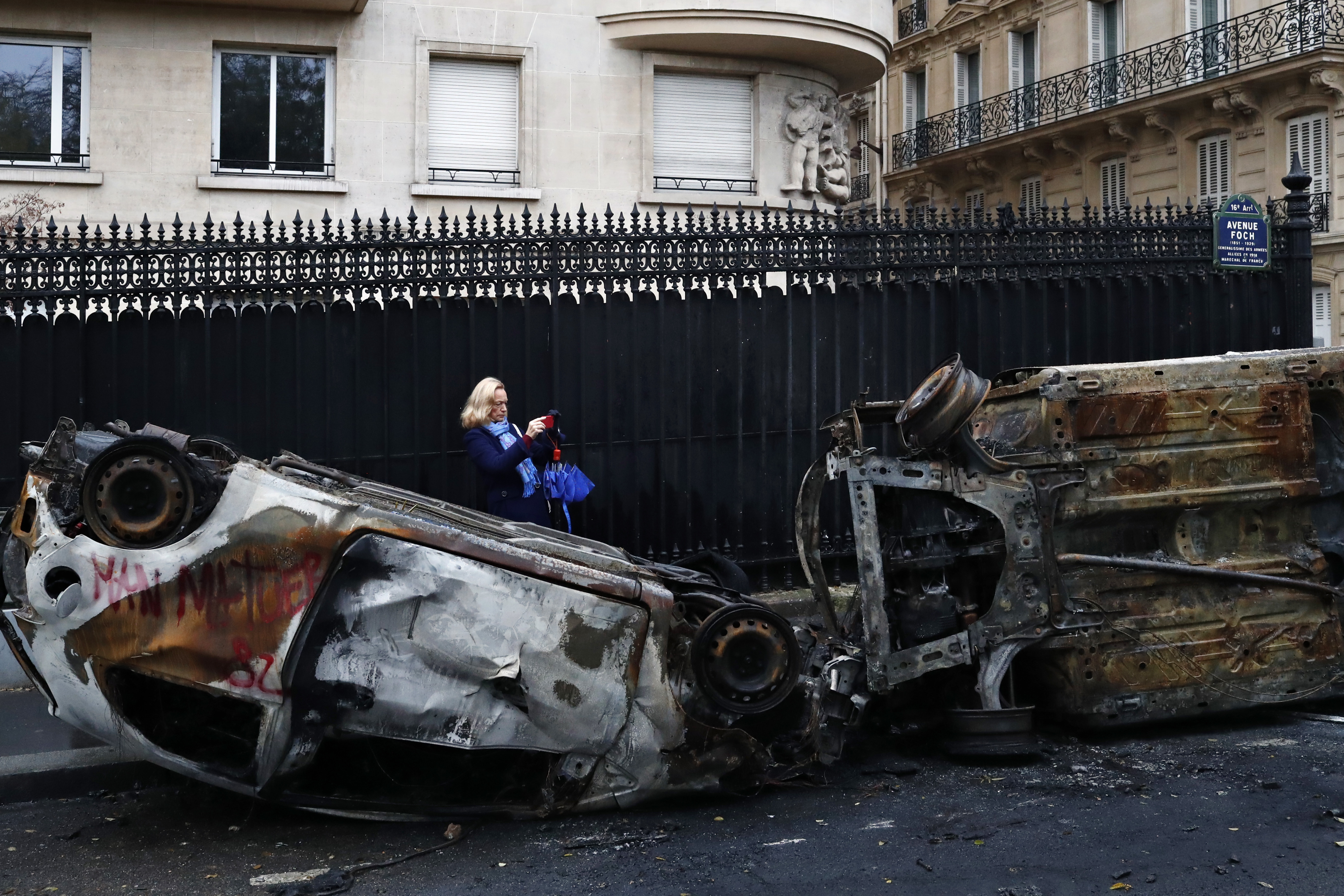 A woman takes a photo of charred cars the day after a demonstration near the Arc de Triomphe in Paris