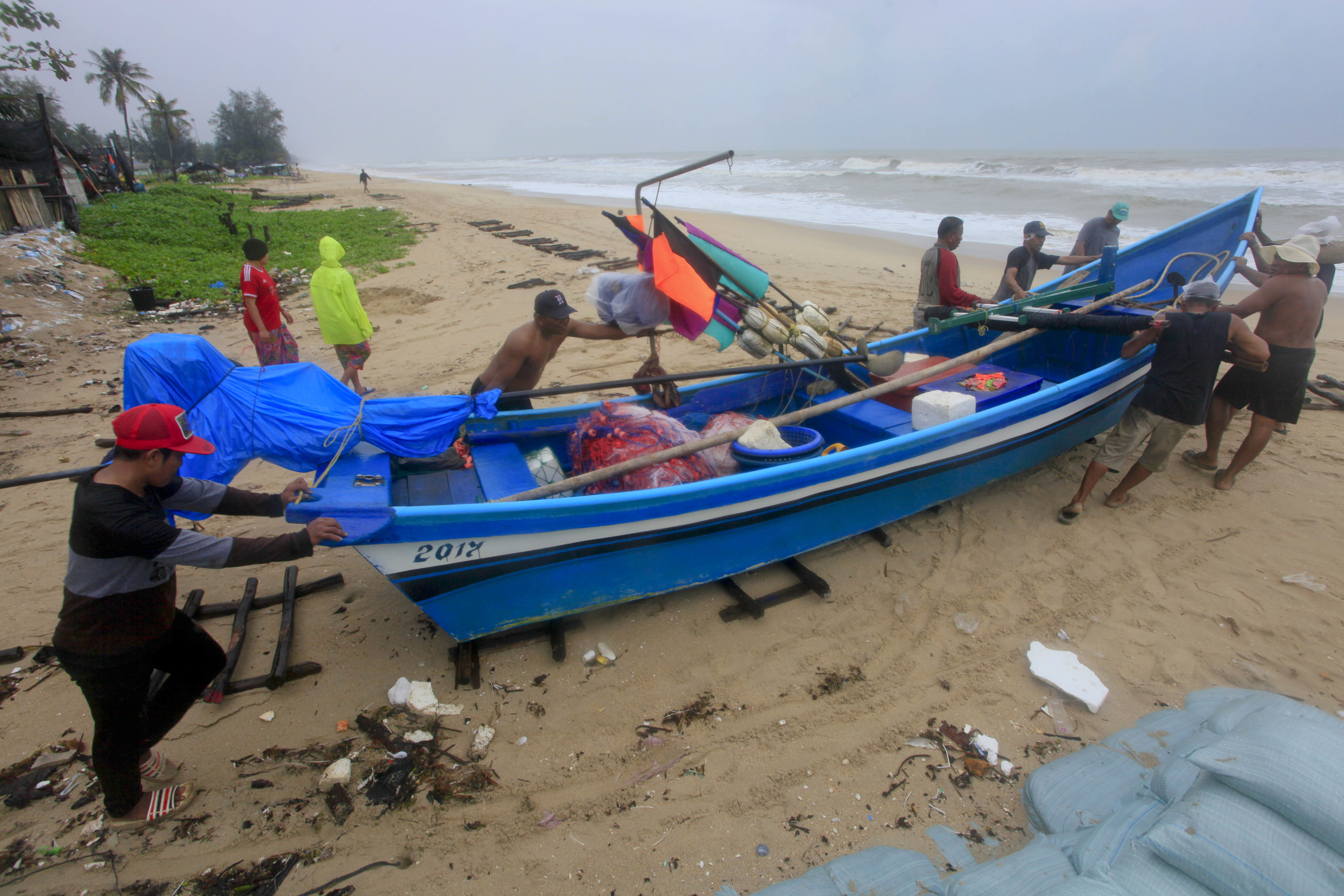 Thai men push a fishing boat off the ocean to a safer location in Songkhla, Thailand