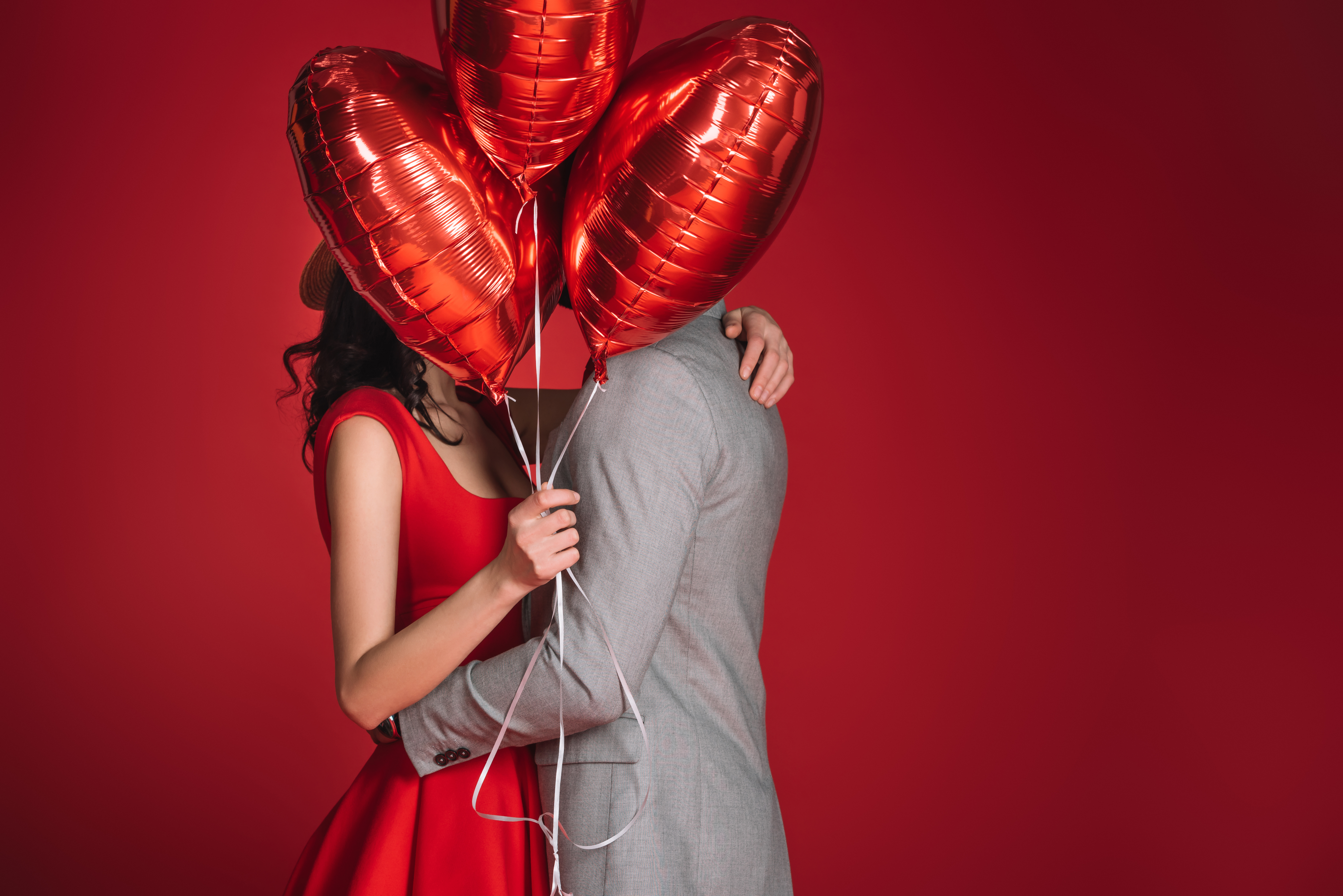 A couple covering their faces with some red balloons