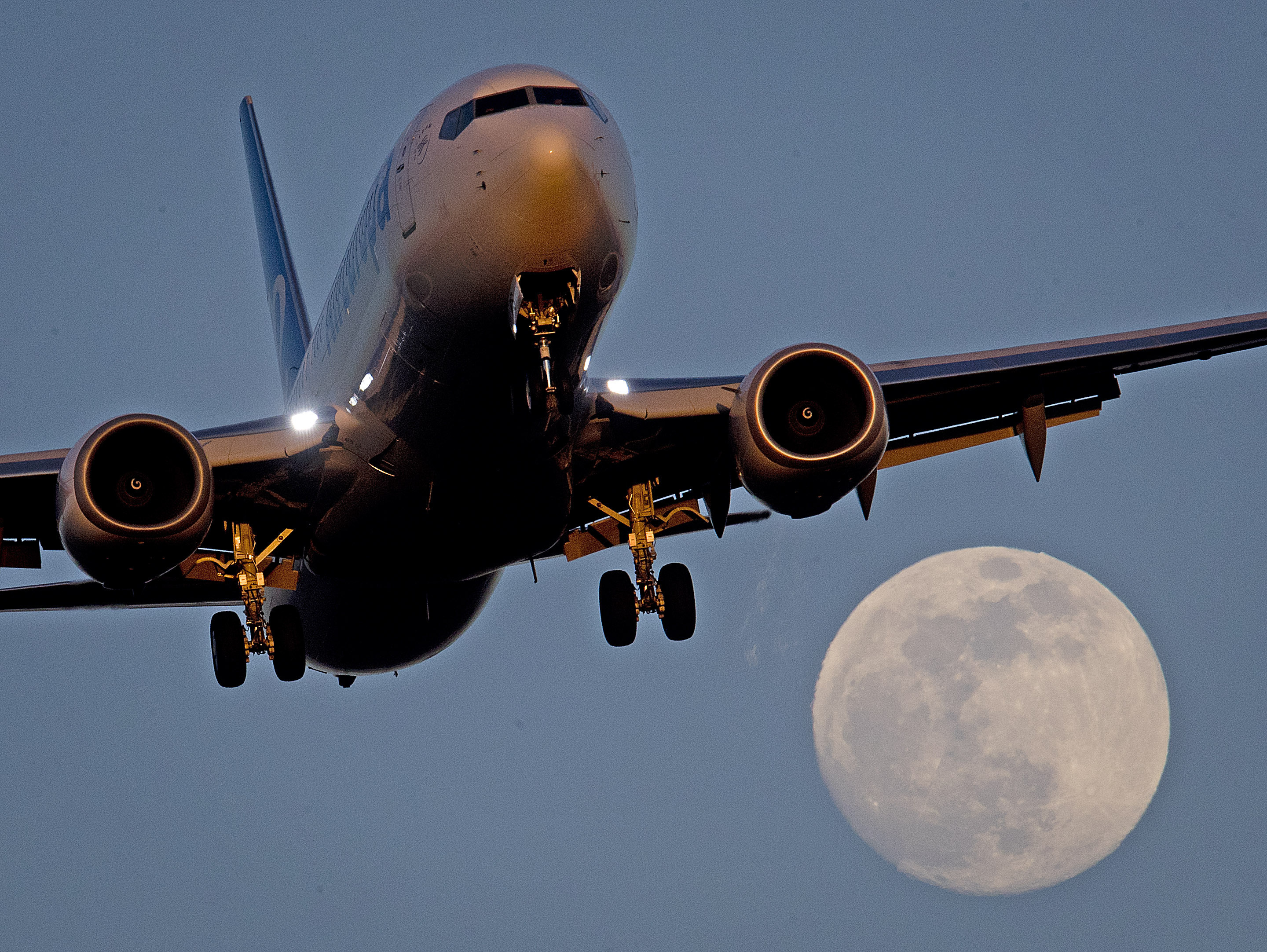An aircraft approaches an airport as the moon rises in Frankfurt, Germany