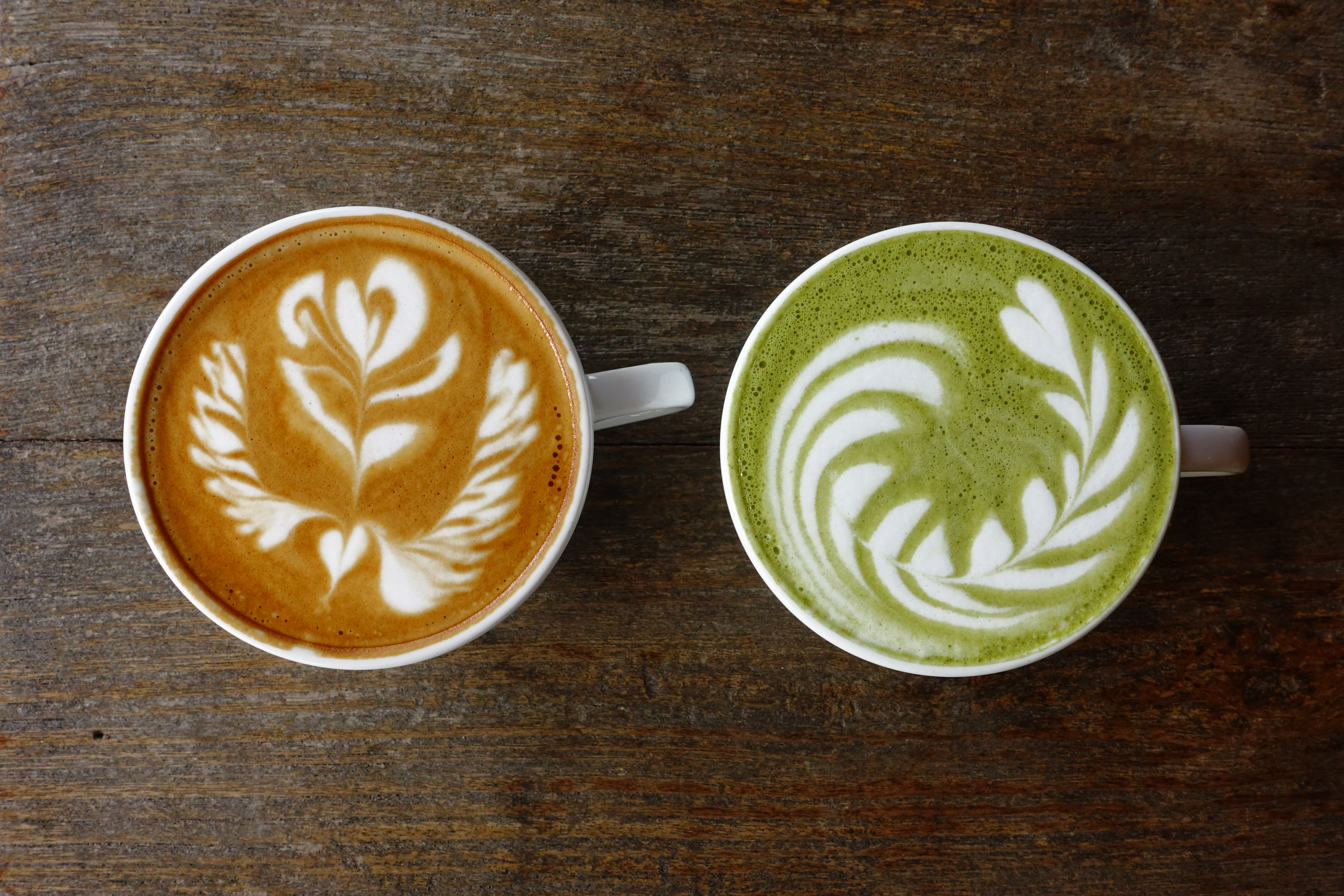 A cup of green tea matcha latte and cup of latte art coffee