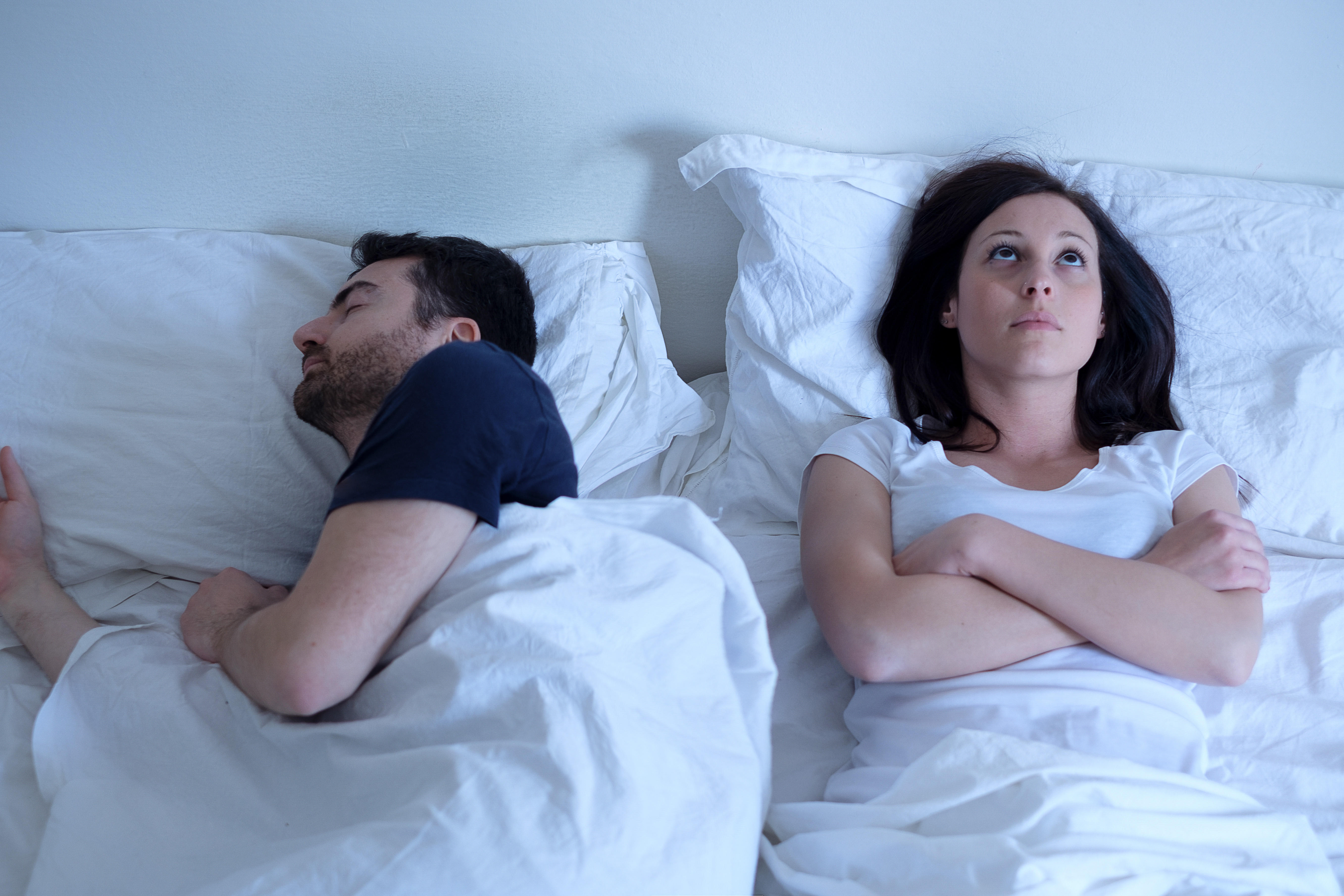 Sad and thoughtful woman awake while husband is sleeping in bed