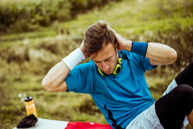 Young handsome athlete sportsman working on his abs outdoors in nature.