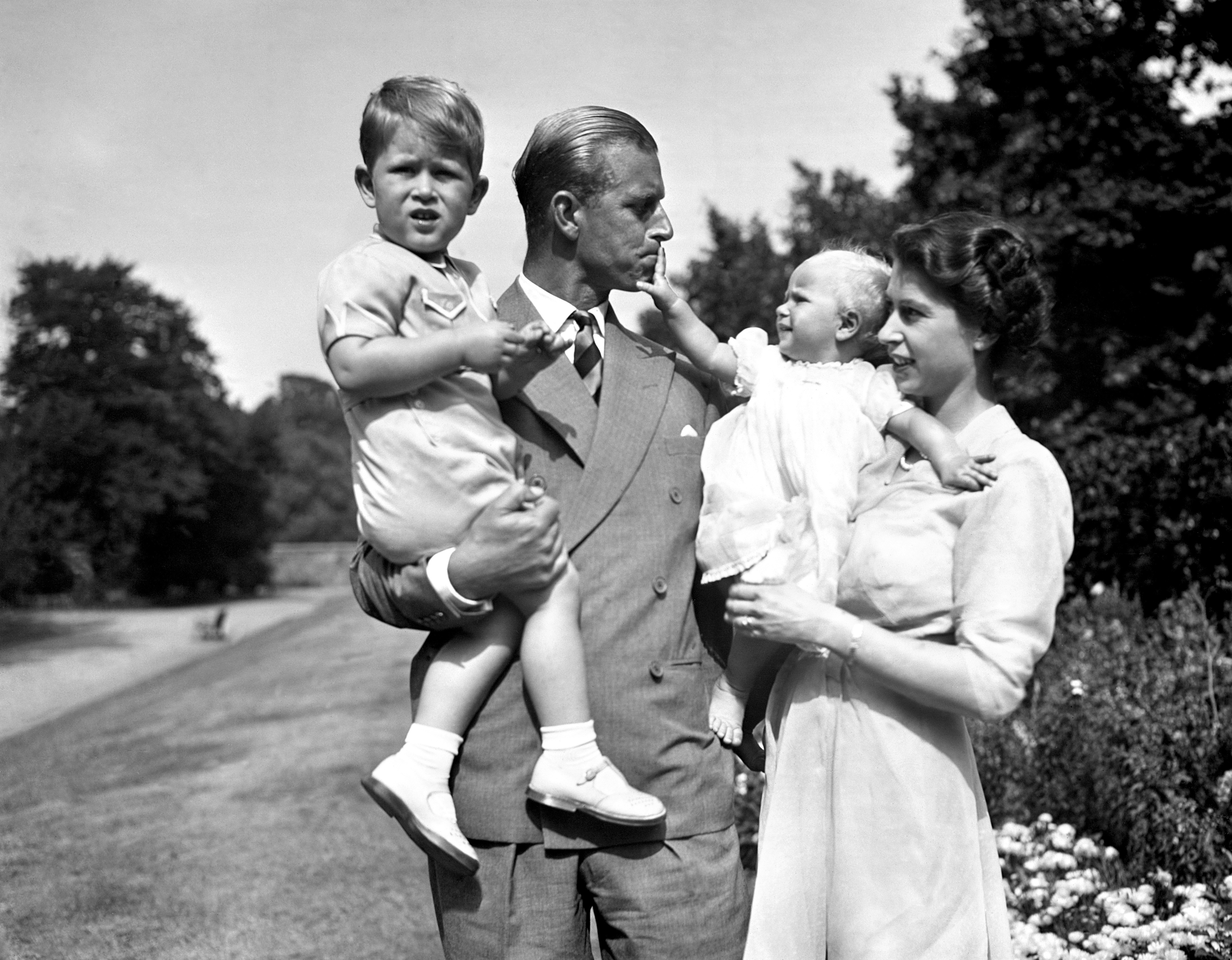 Anne in the arms of Princess Elizabeth, with the Duke of Edinburgh, holding Charles, in the grounds of Clarence House in 1951 