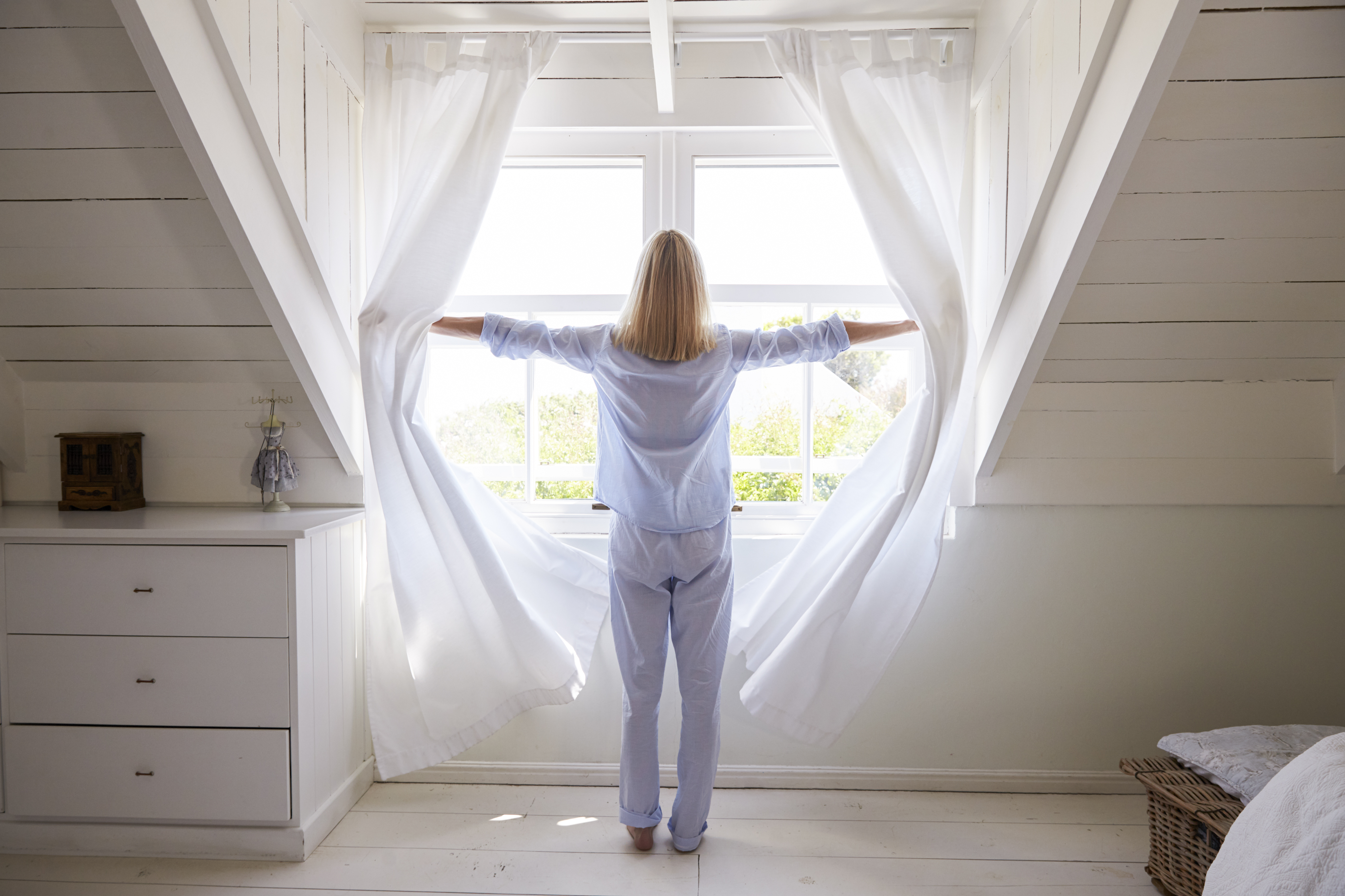 Rear View Of Woman Opening Curtains And Looking Out Of Window