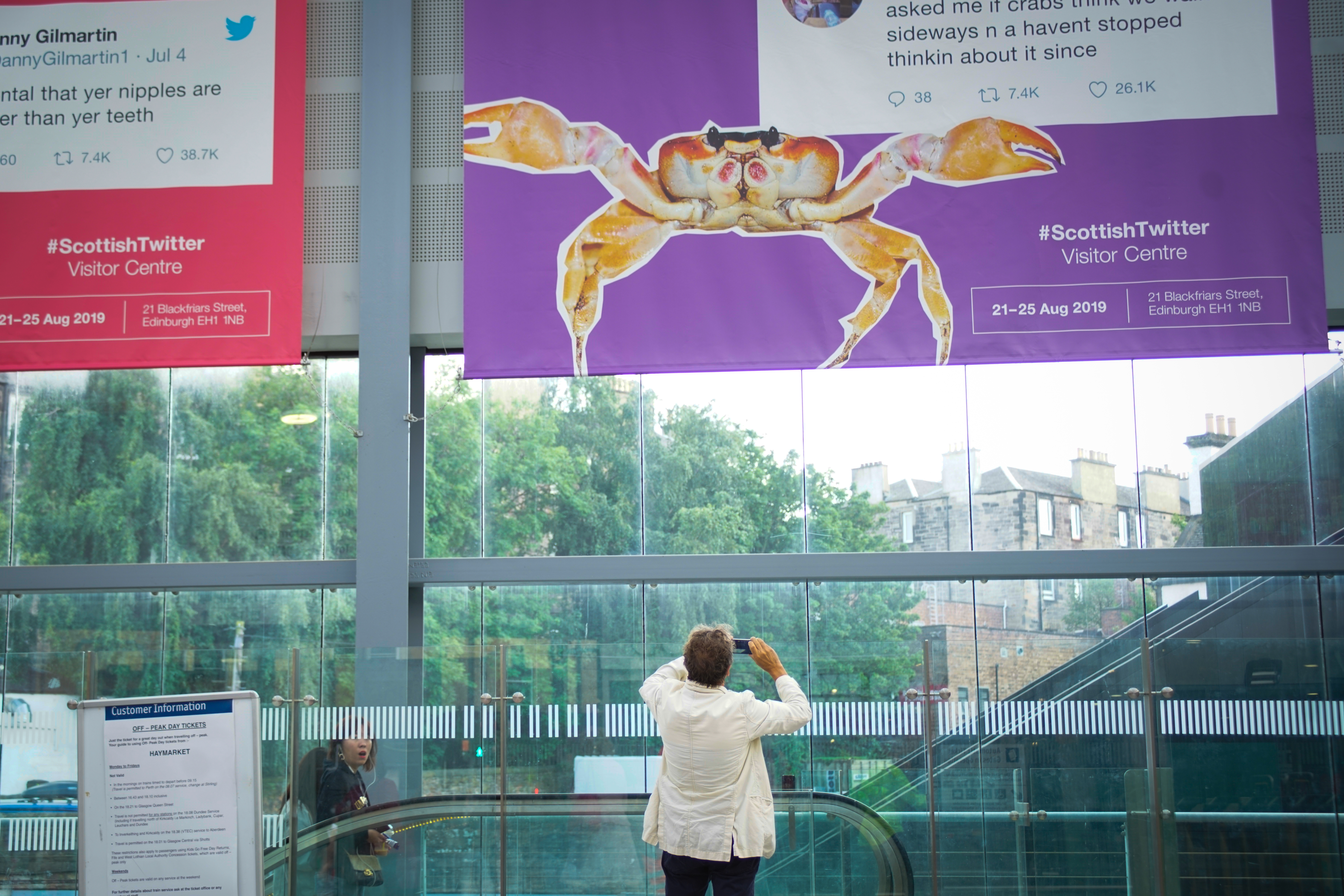 A member of the general public takes a photo of a poster of a tweet in Haymarket, Scotland