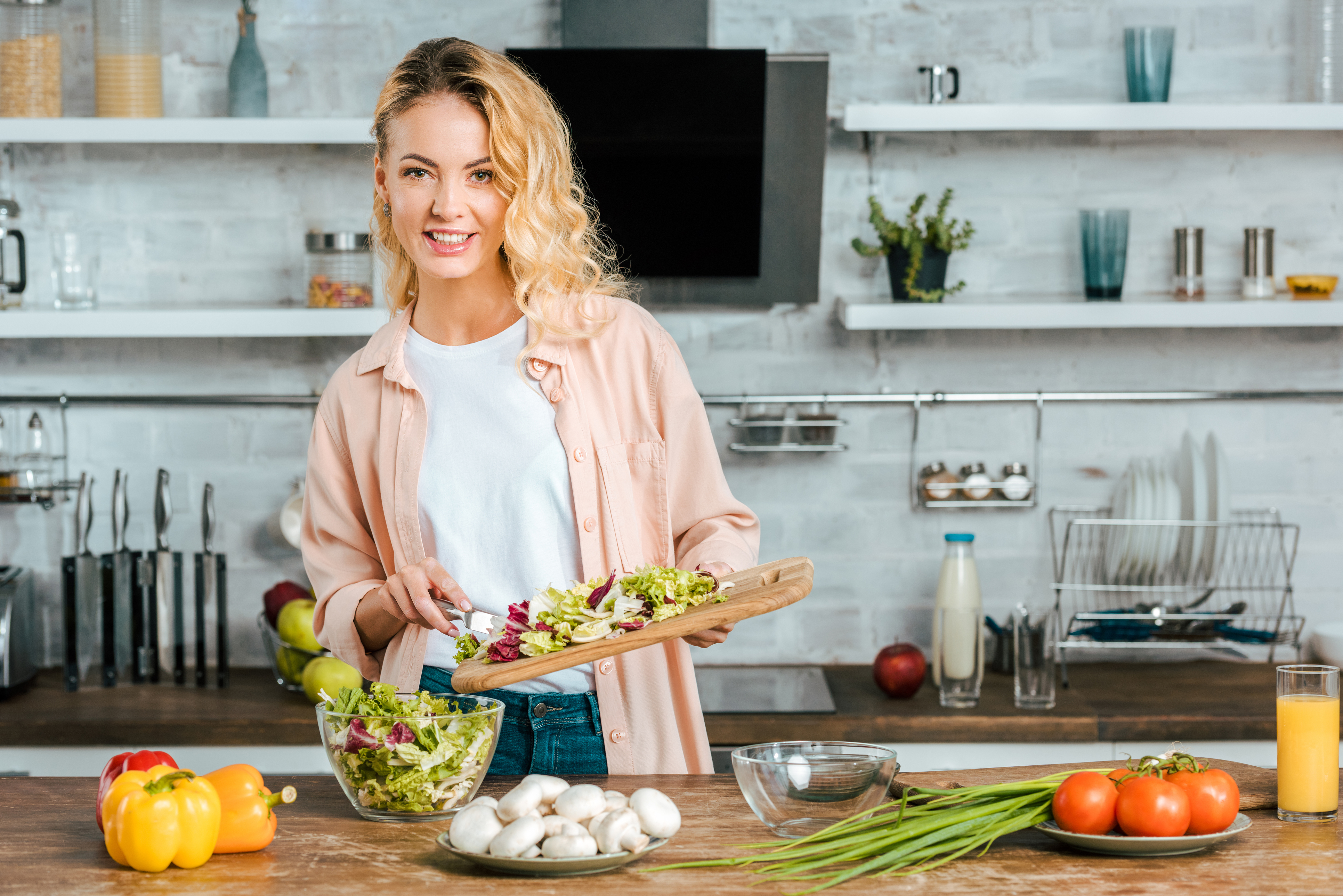 happy young woman with cutting board of cut lettuce at kitchen