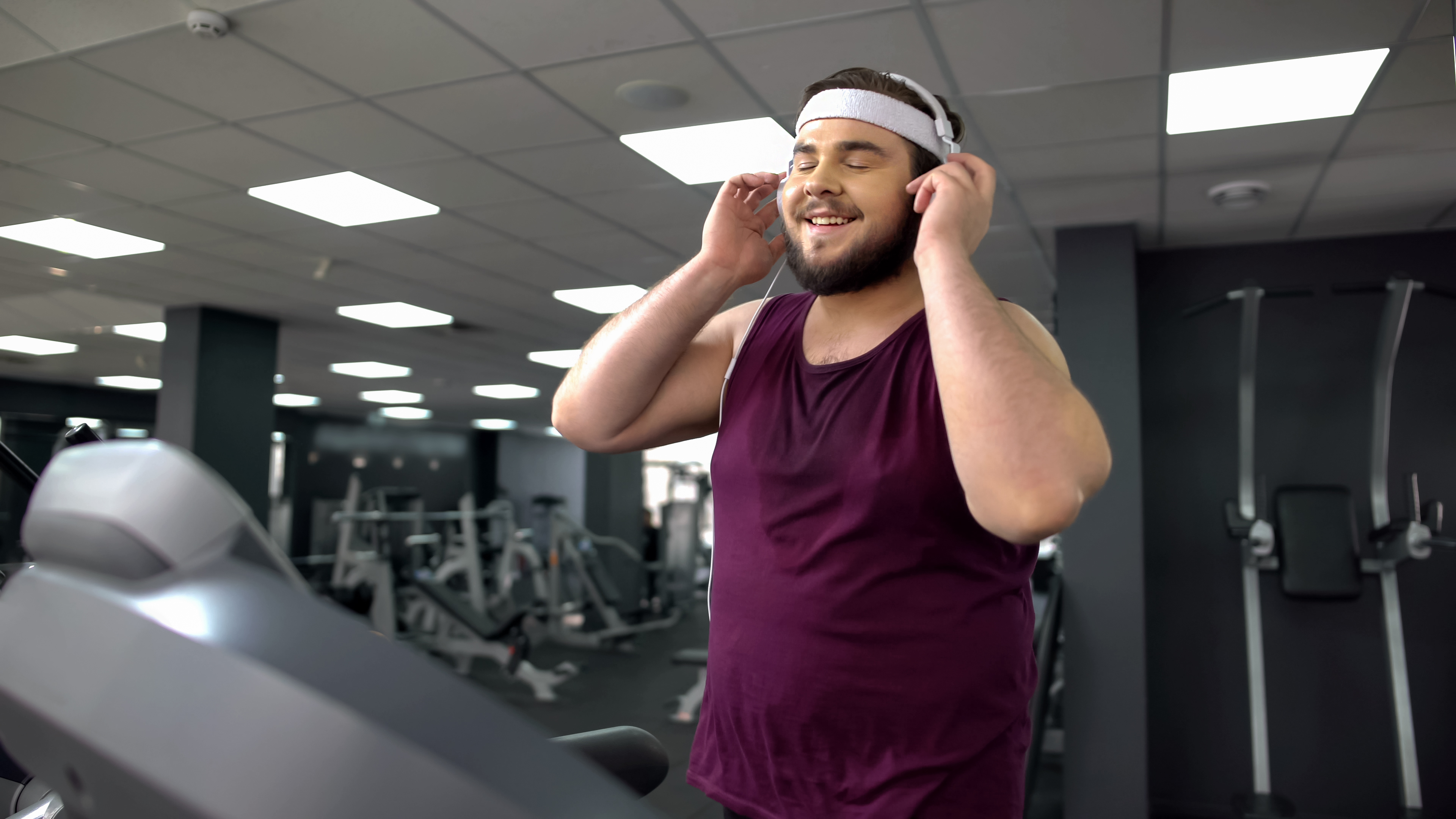 Fat man putting on headset and listening to music during jogging on treadmill