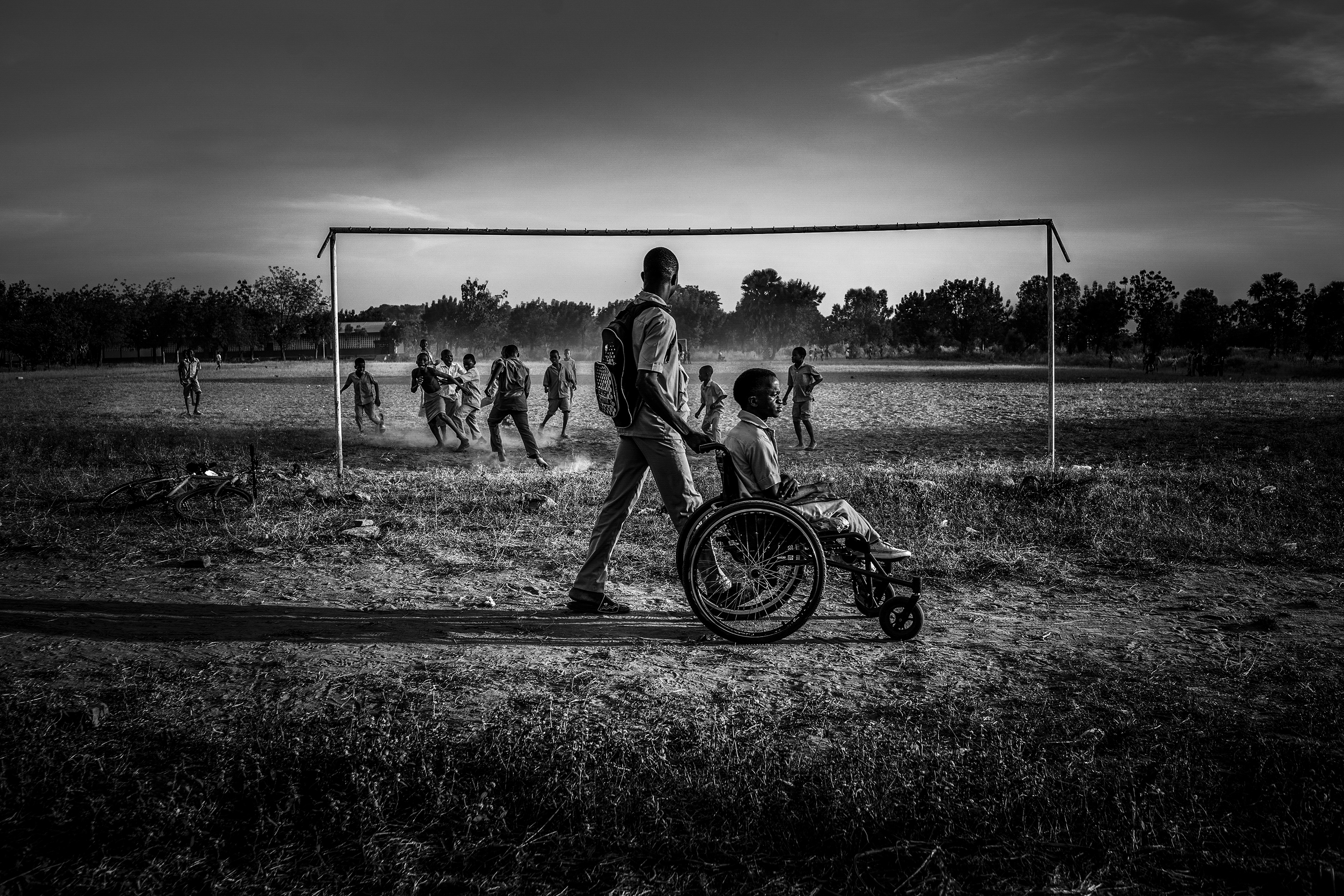 A child eing pushed in a wheelchair against a backdrop of others playing football