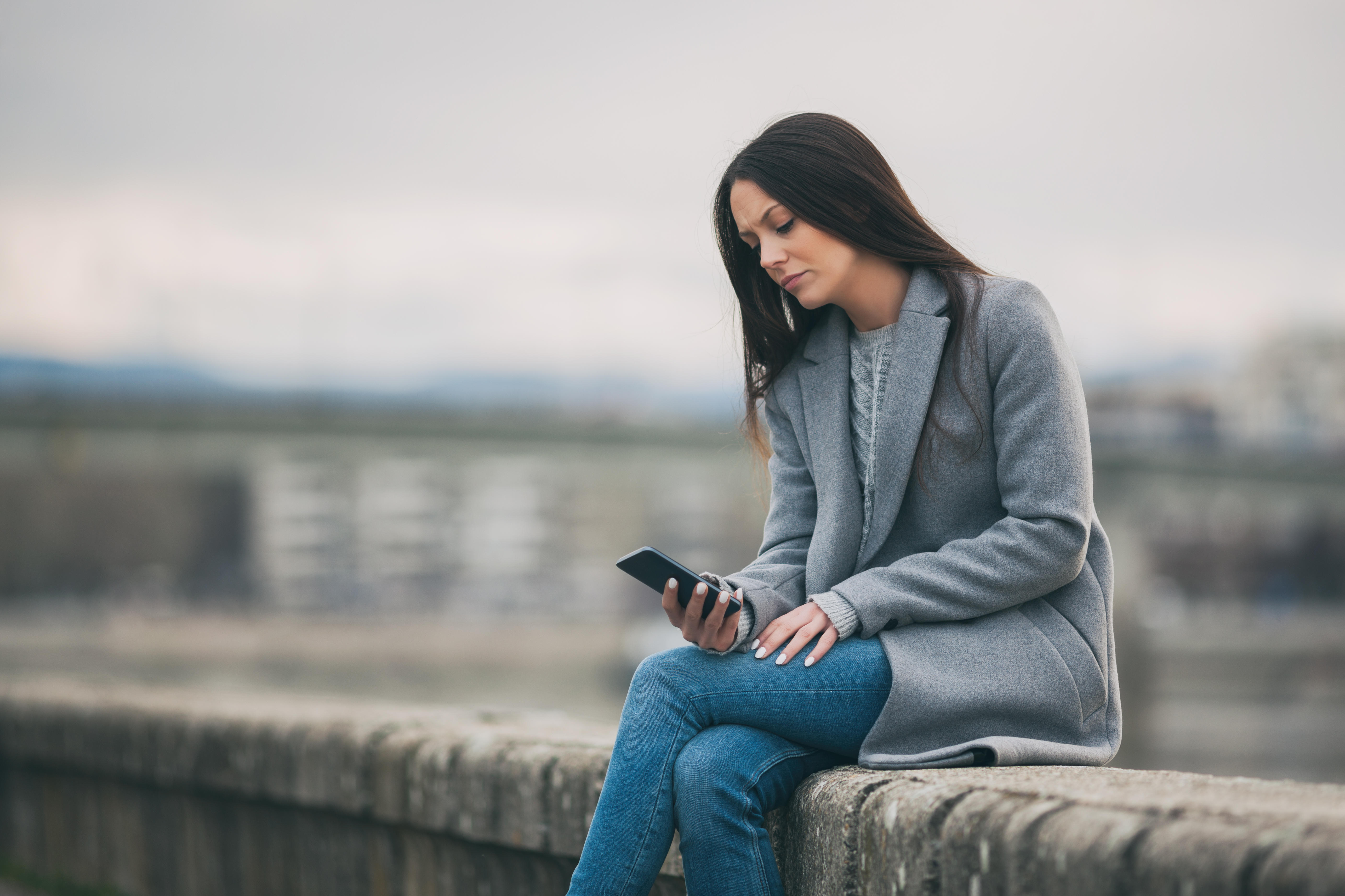 Woman sat on a wall looking at phone