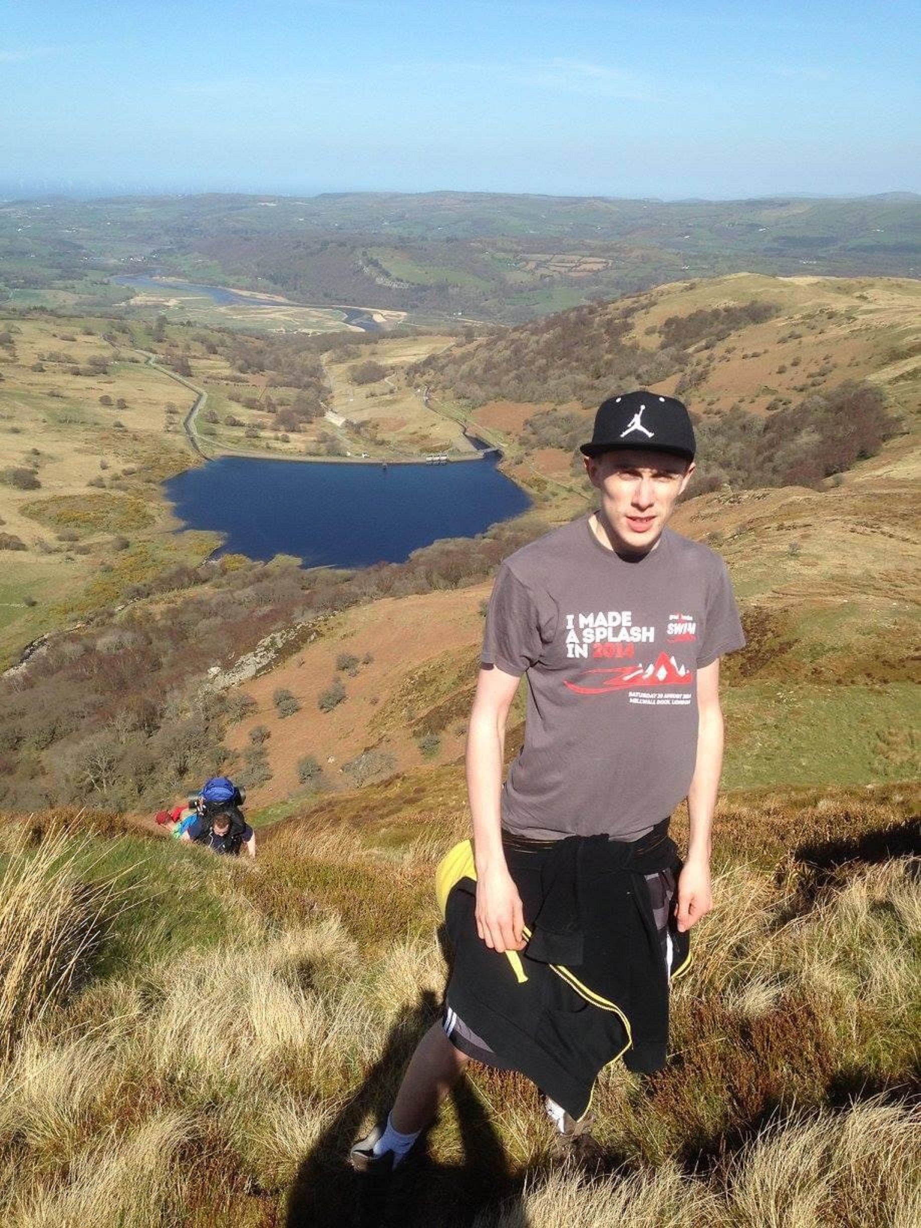 Jack Bayley, 20, stands on a hill, wearing a grey t-shirt and a black cap