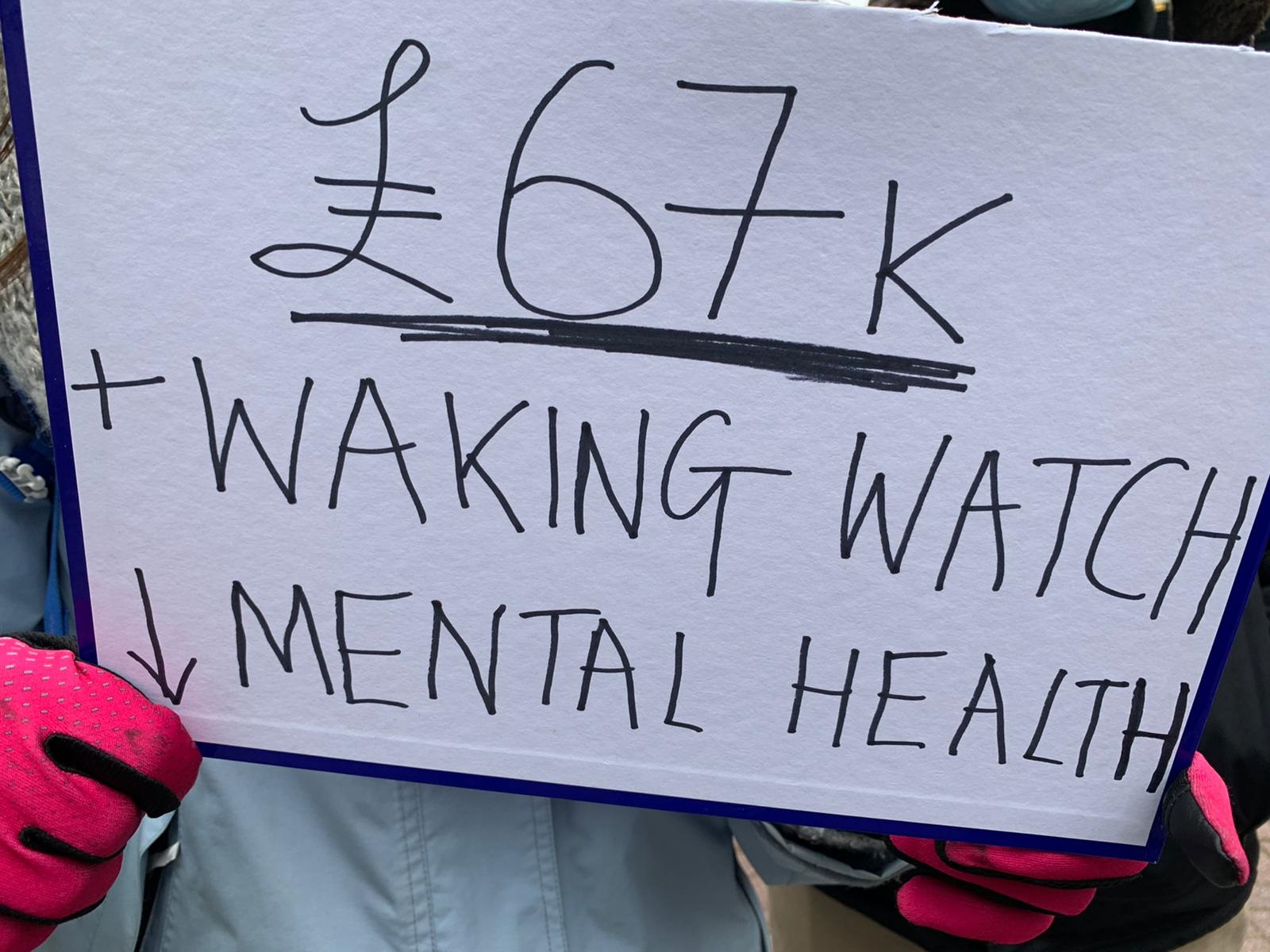 A sign held by a protester, protesting against the cost of waking watches - it says '£67k + Waking Watch - Mental Health'