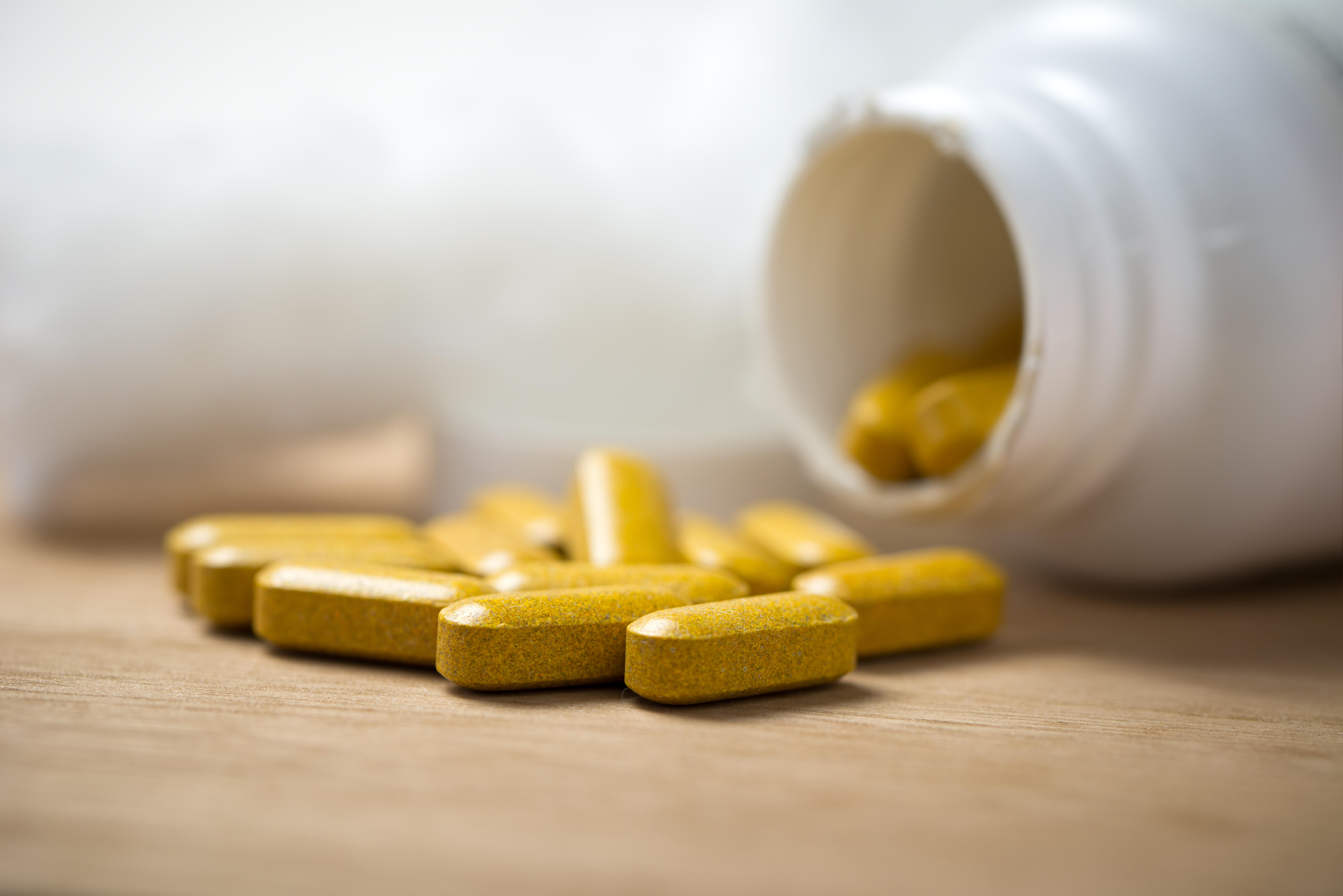 Dietary supplement tablets pouring out of container