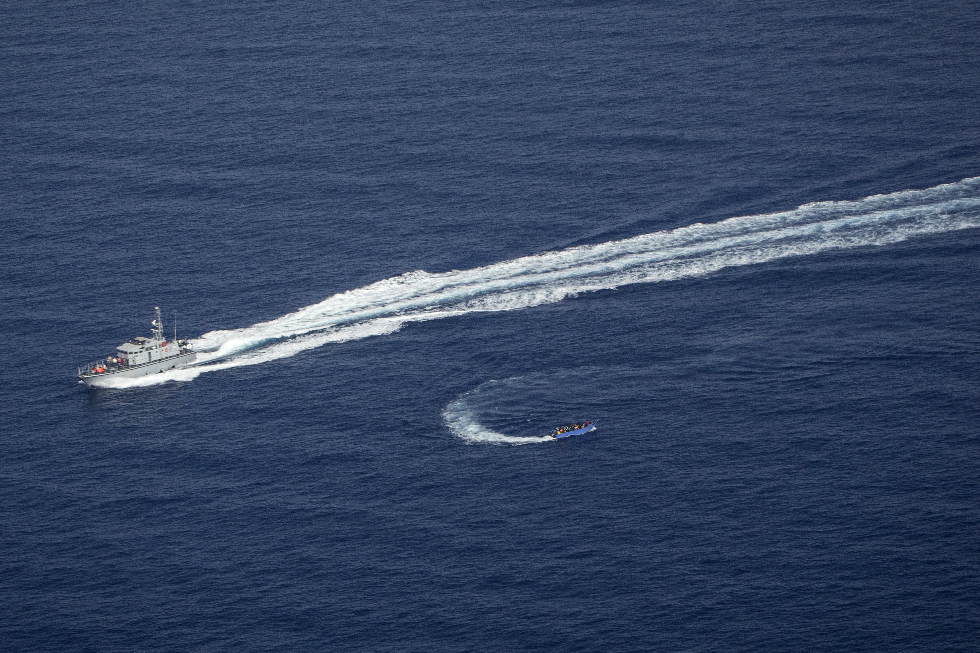An overcrowded migrant boat, bottom, tries to escape from the Libyan coast guard in the Mediterranean Sea
