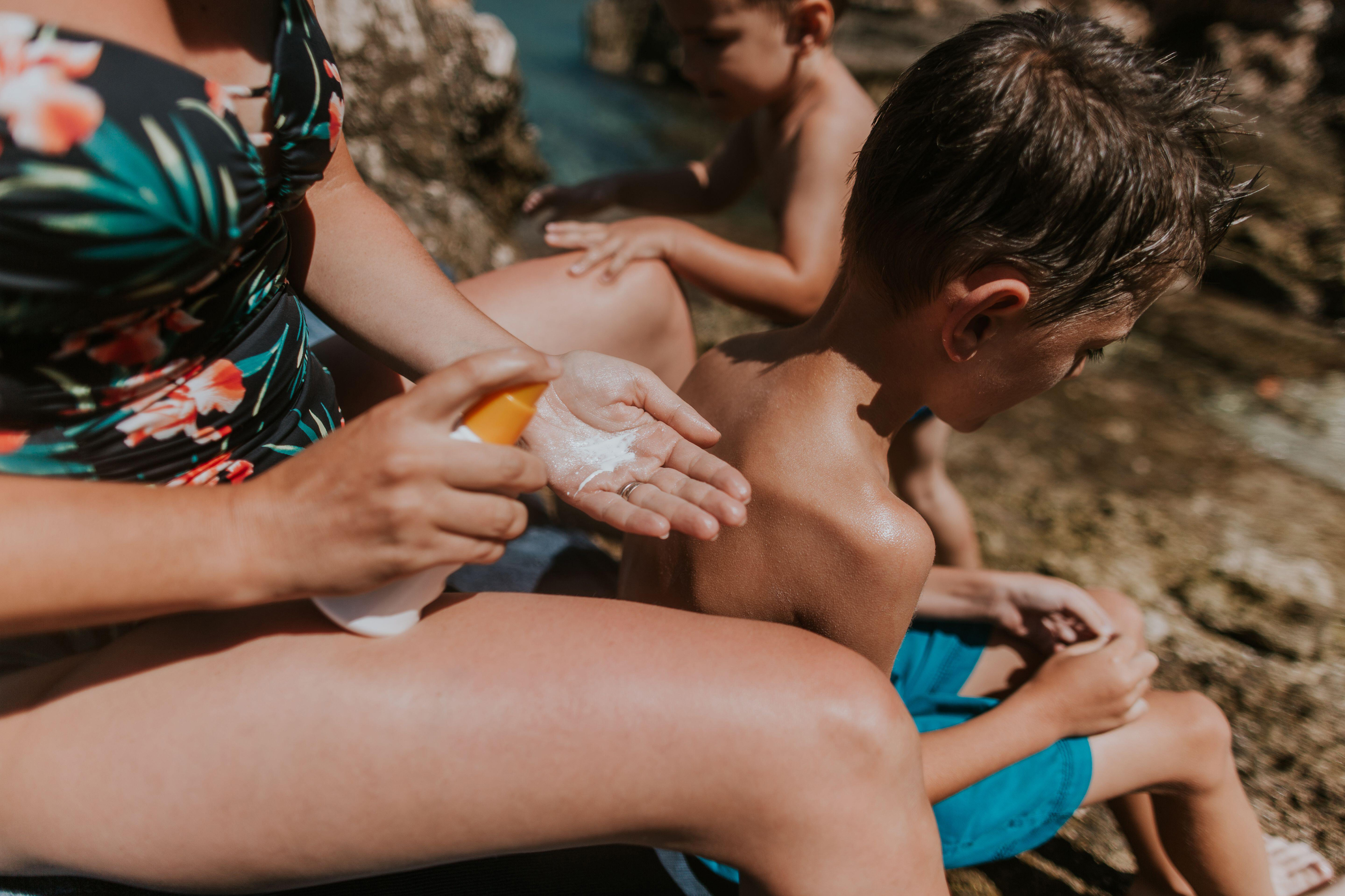 Mother applying sunscreen lotion on her child on beach