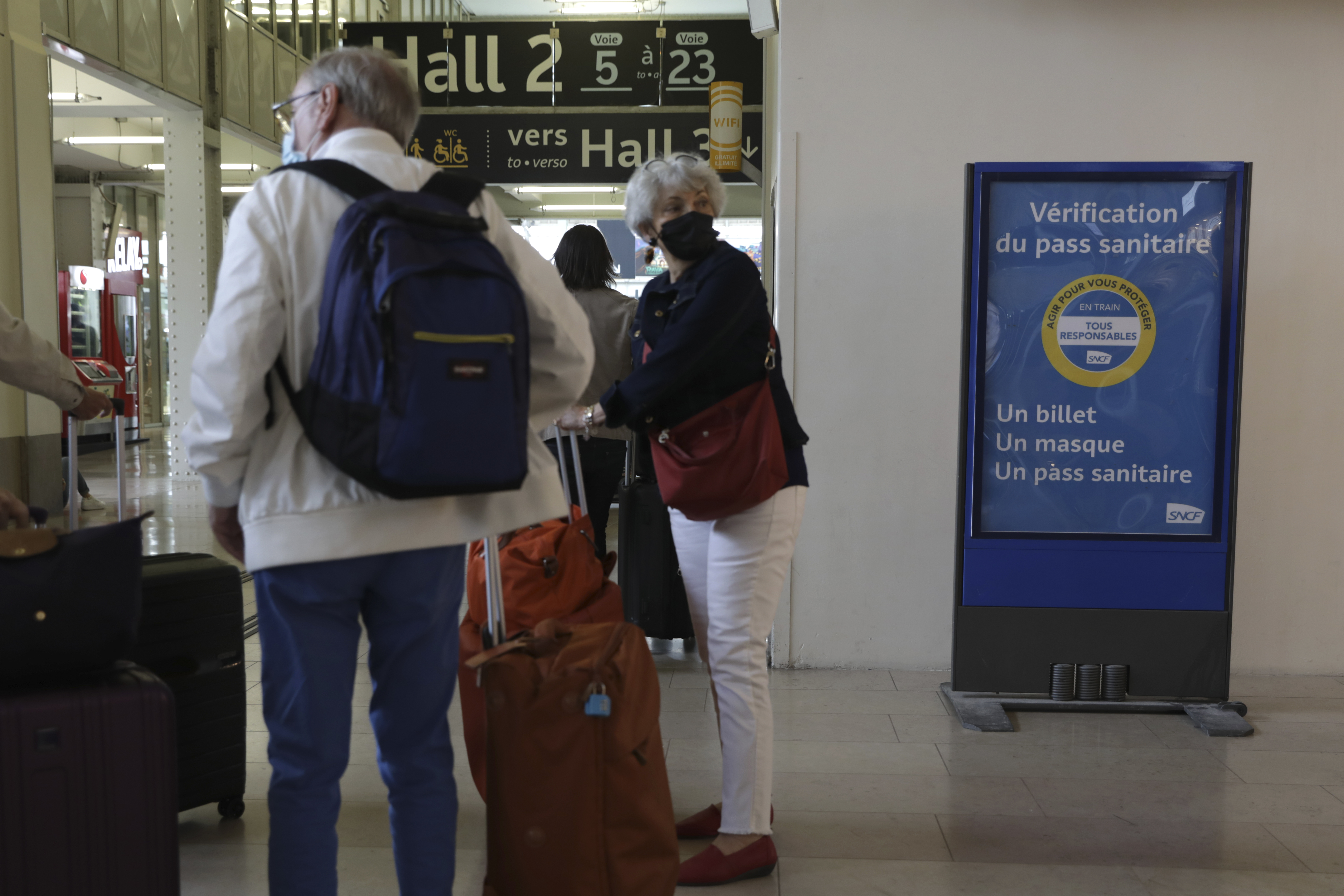 People arrive at the Gare de Lyon train station where a sign reads 'A ticket, a mask, a health pass, in Paris