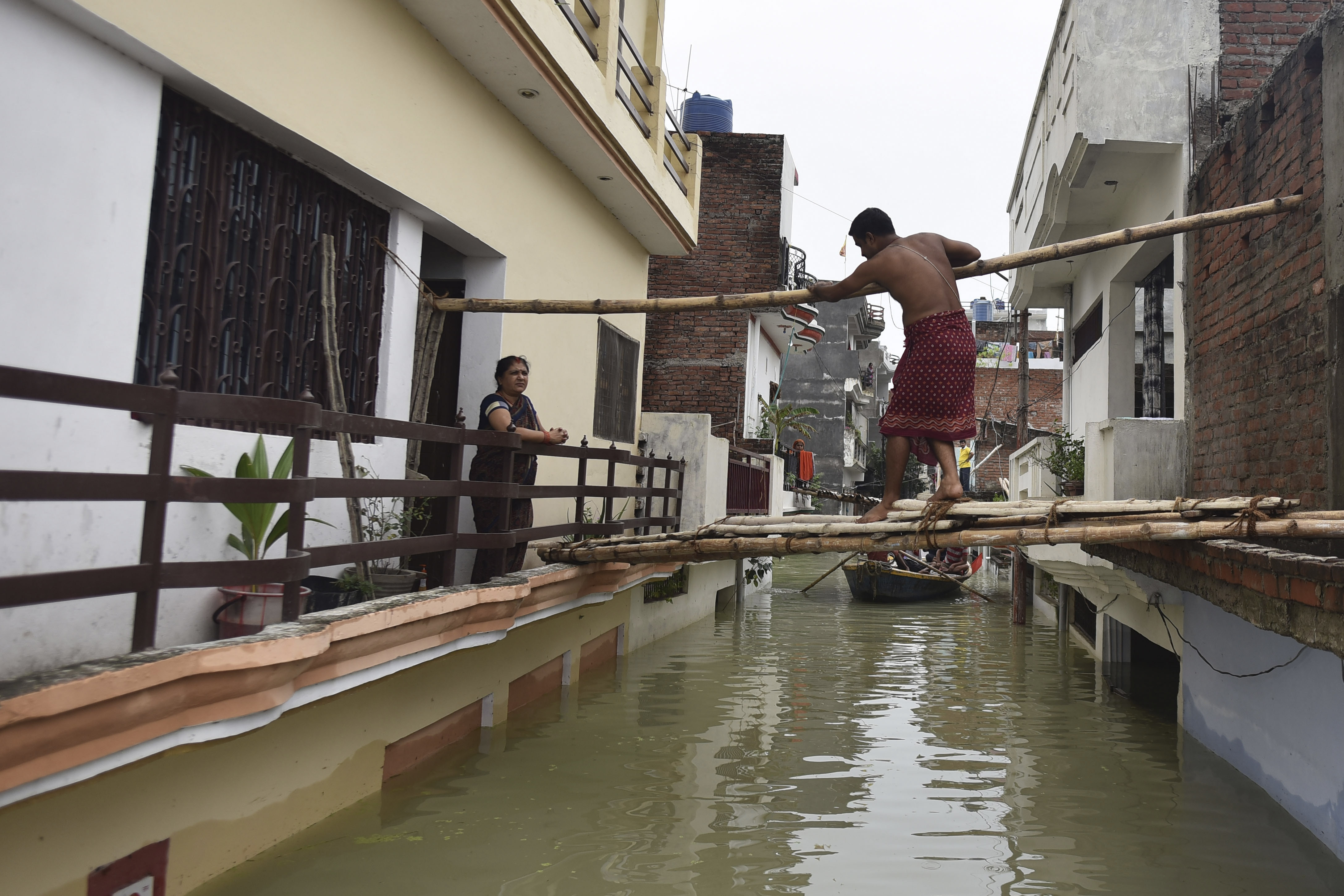 A man walks on a makeshift bamboo bridge between flooded houses