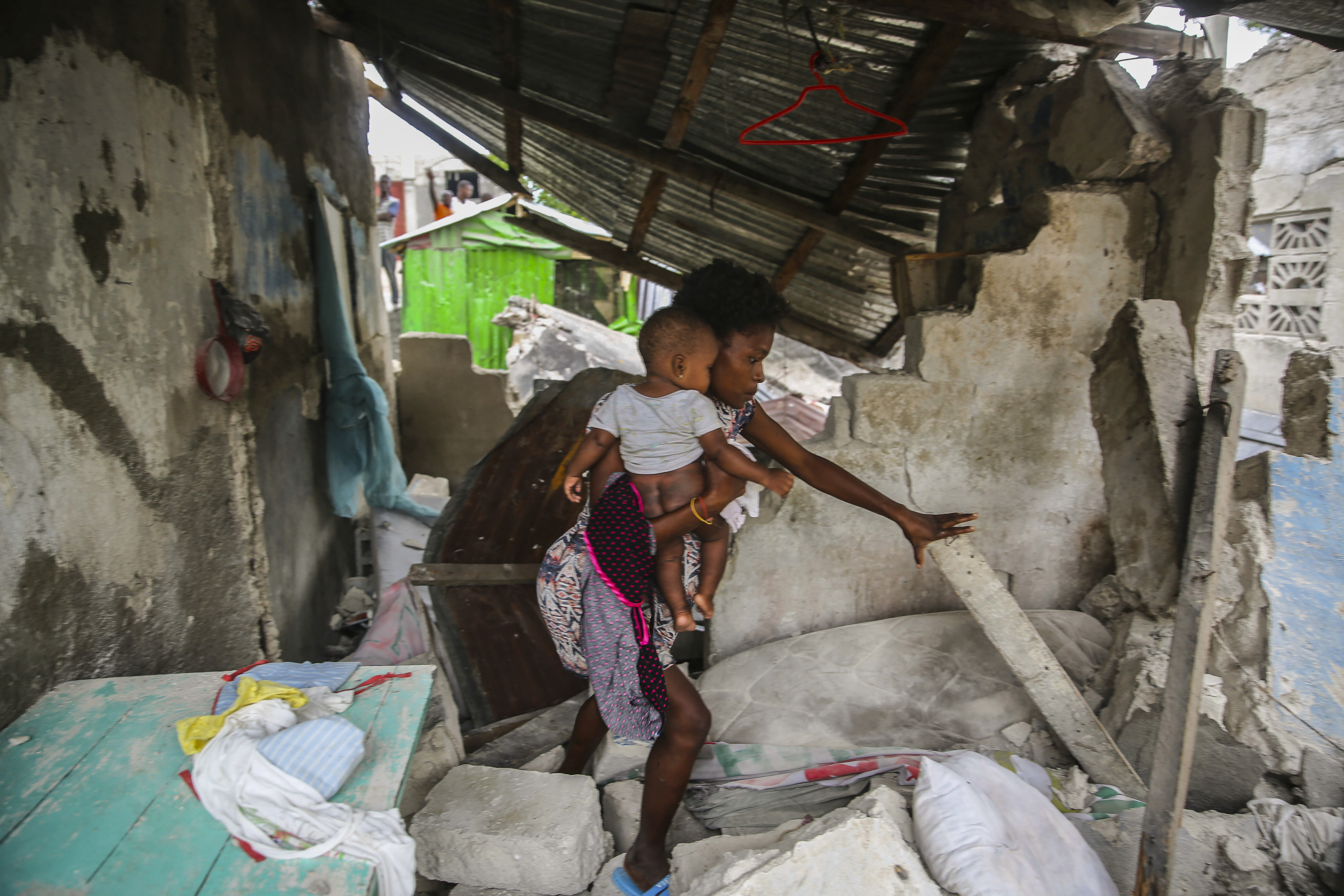 A woman carries her child as she walks in the remains of her home destroyed by Saturday´s  7.2 magnitude earthquake in Les Cayes, Haiti