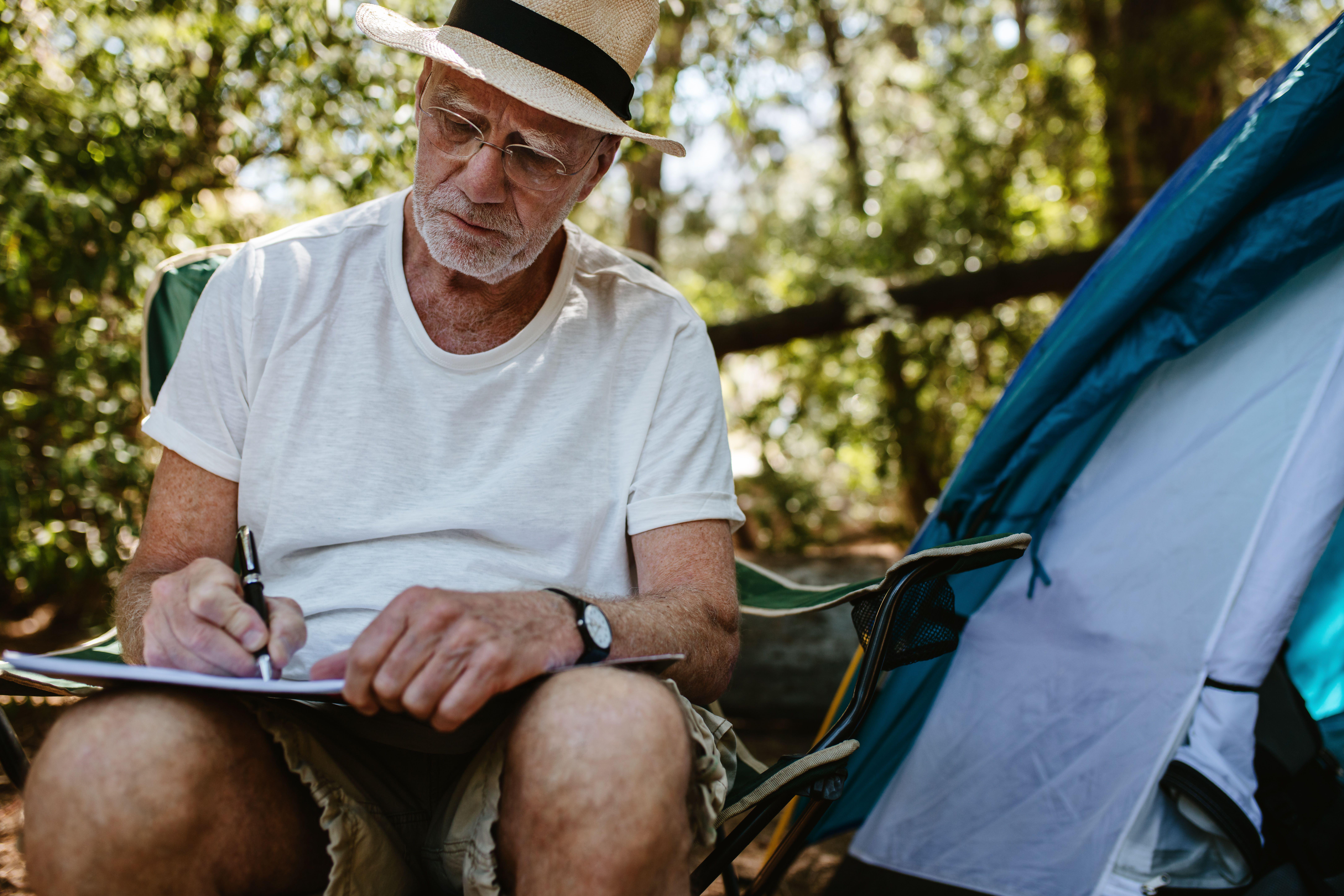Senior man sitting in front of a tent and writing in a book