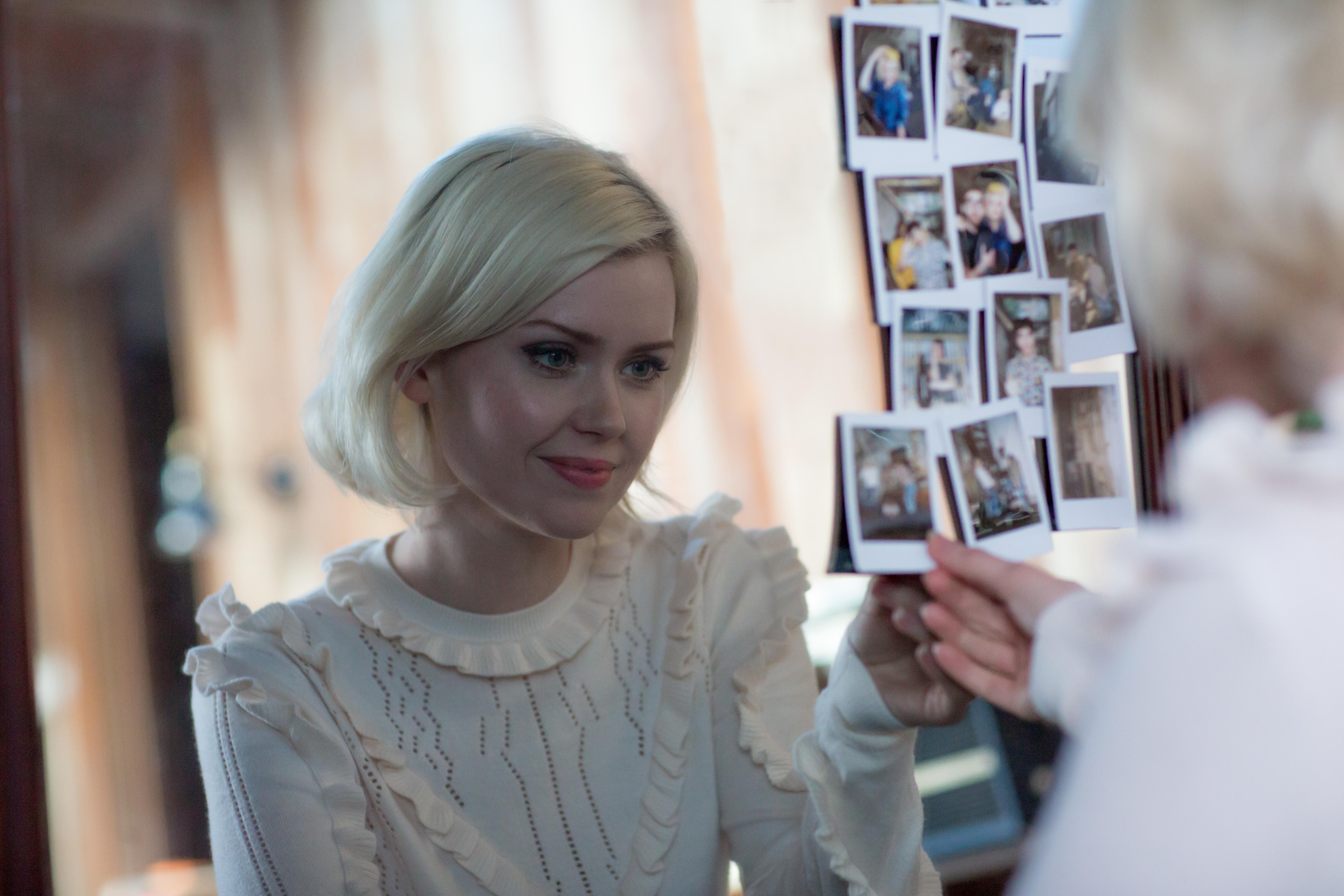 Woman looking at polaroid photos hanging on a mirror