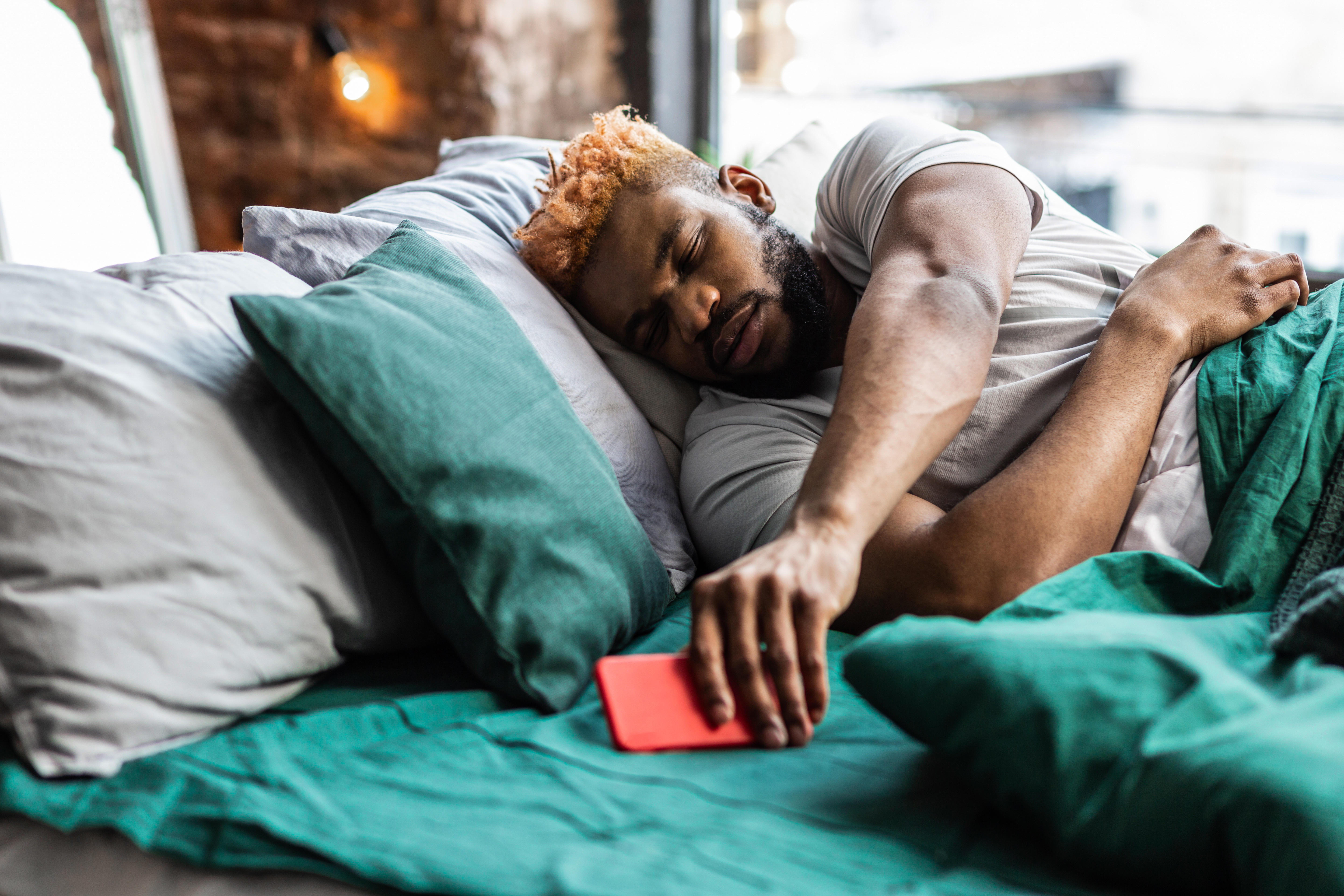 Man lying in bed reaching for his phone