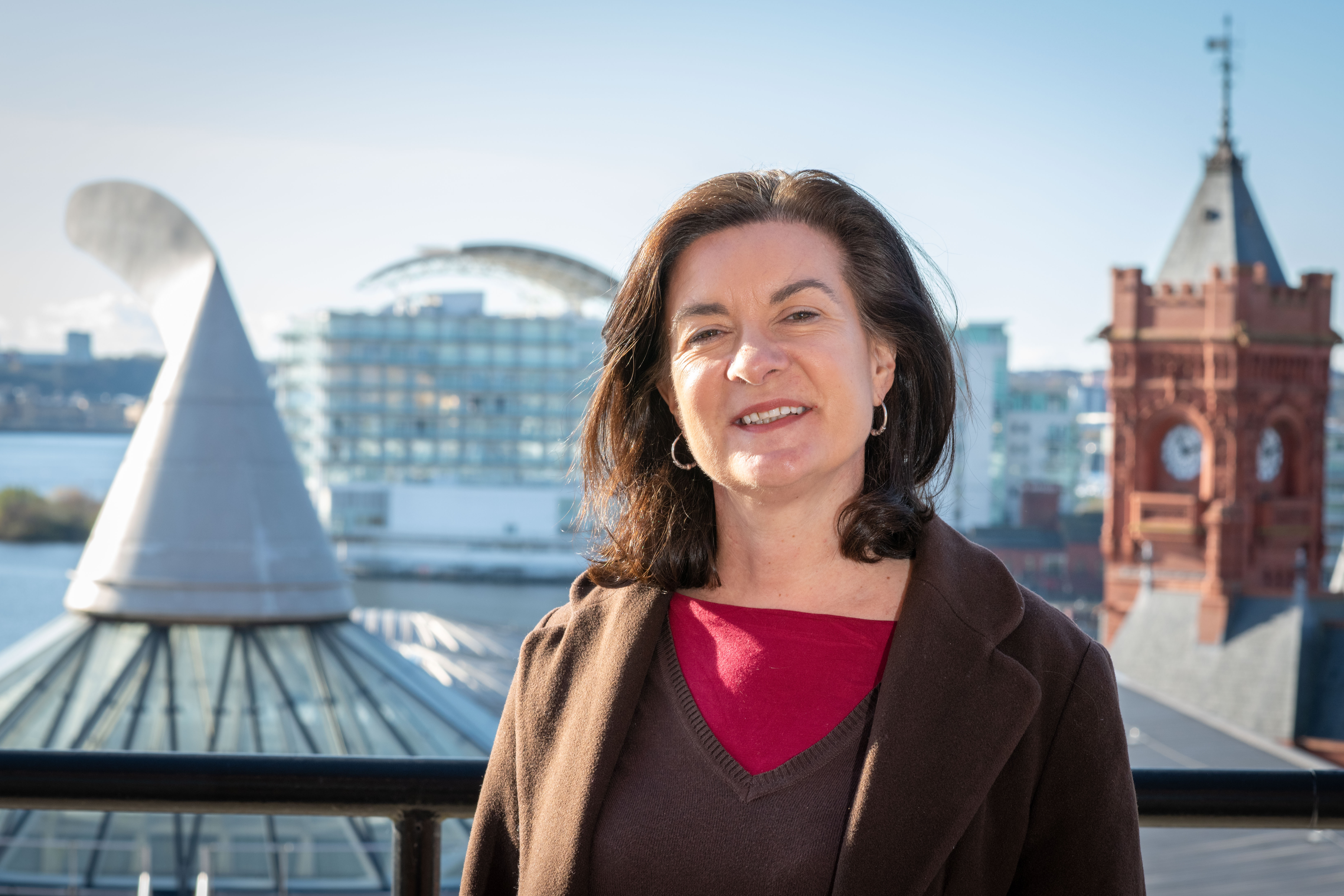 Eluned Morgan smiling while posing for photos on a rooftop, with buildings and blue skies behind her