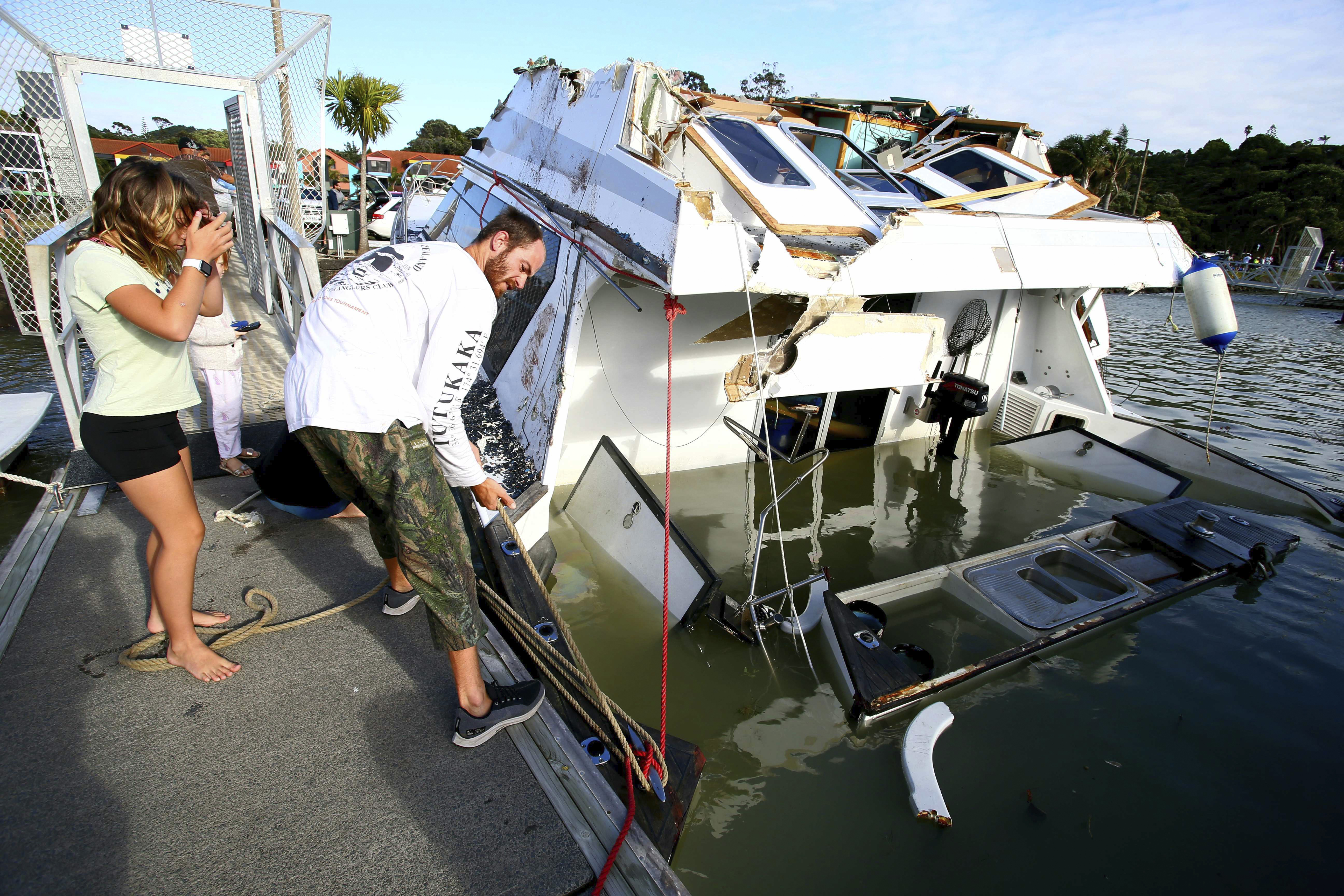 A couple look at a damaged boat in a marina at Tutukaka, New Zealand after waves from a volcano eruption swept into the marina