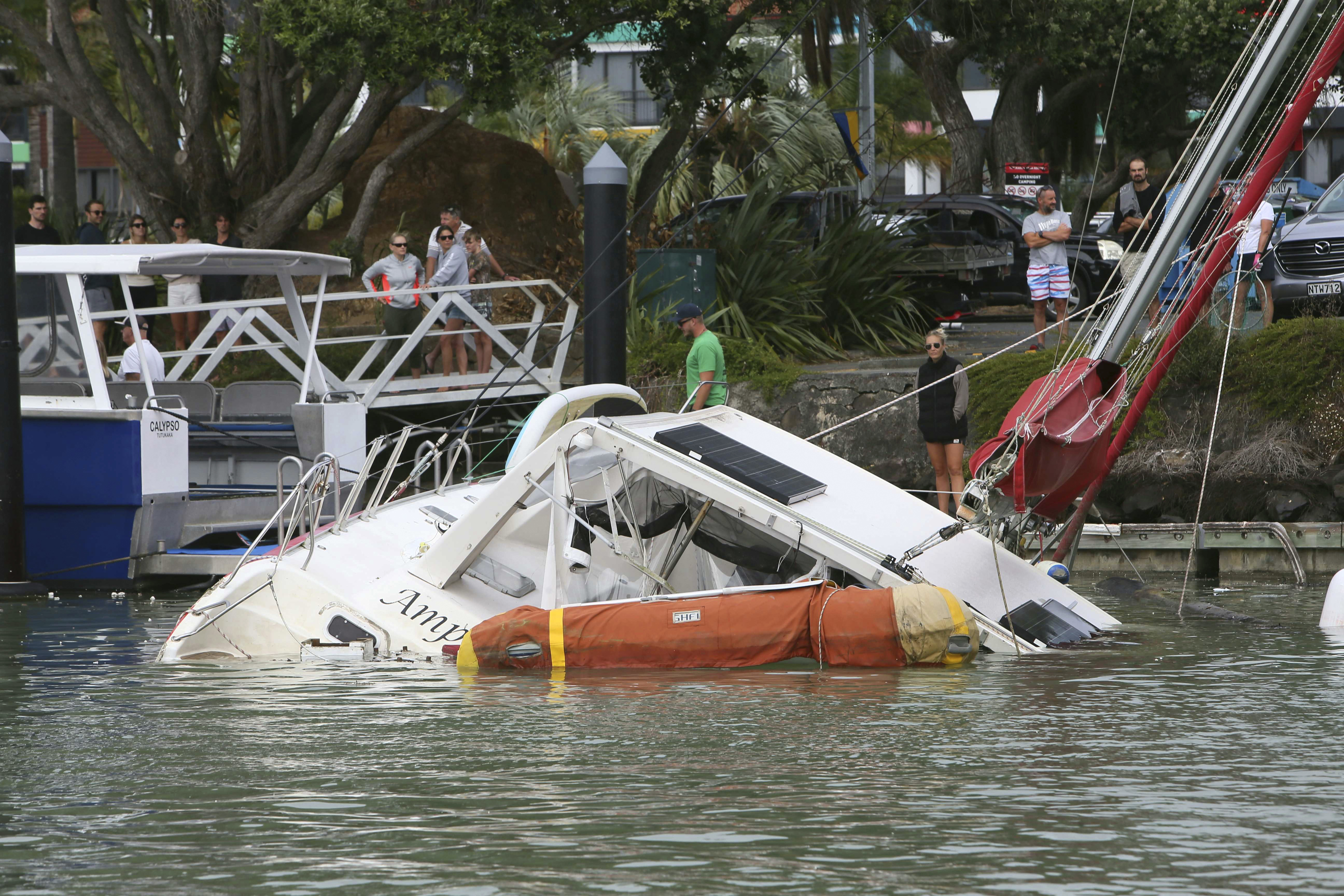 People look at a damaged boat in a marina at Tutukaka, New Zealand after waves from a volcano eruption swept into the marina